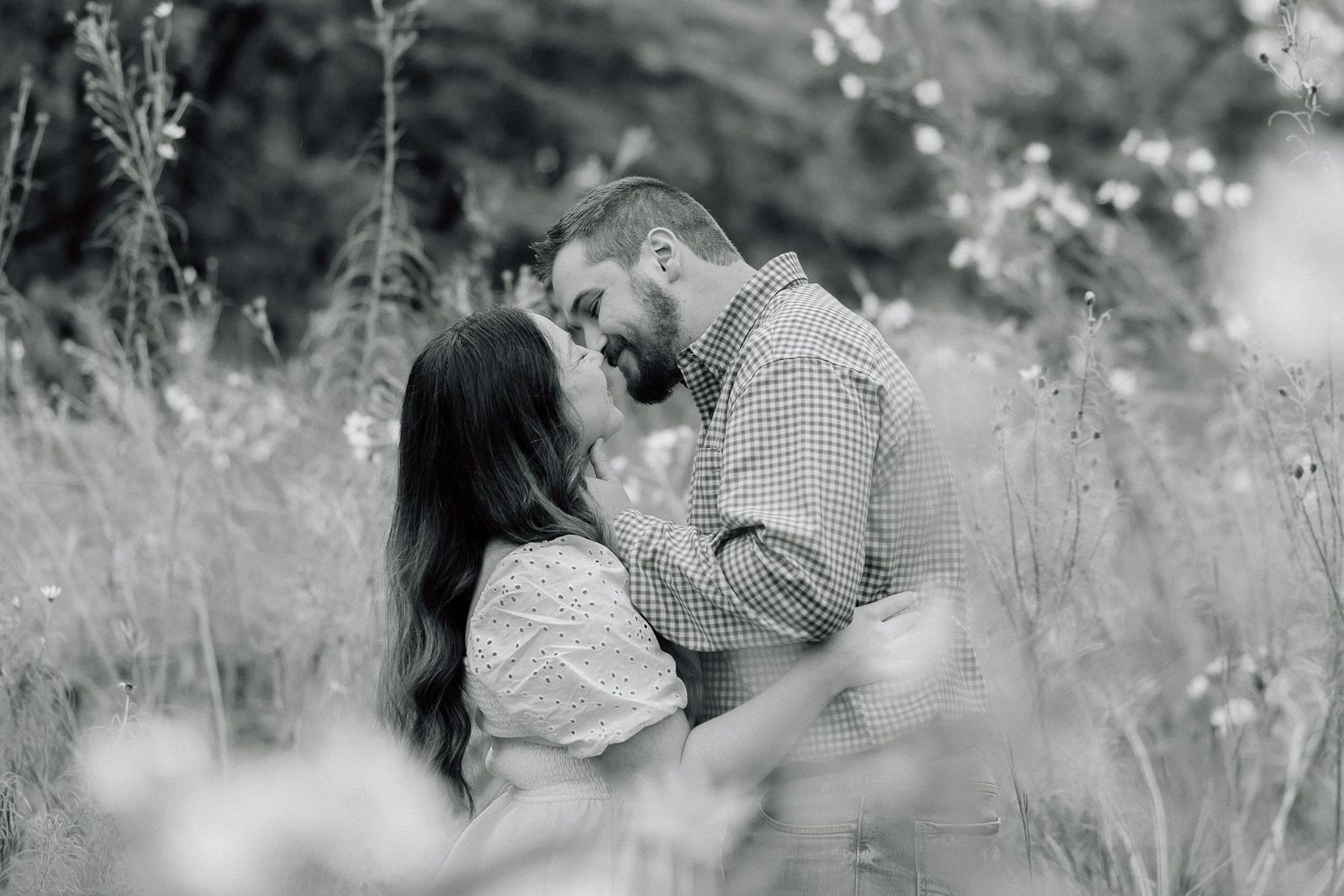 A black and white portrait of a couple embracing in a wild meadow.