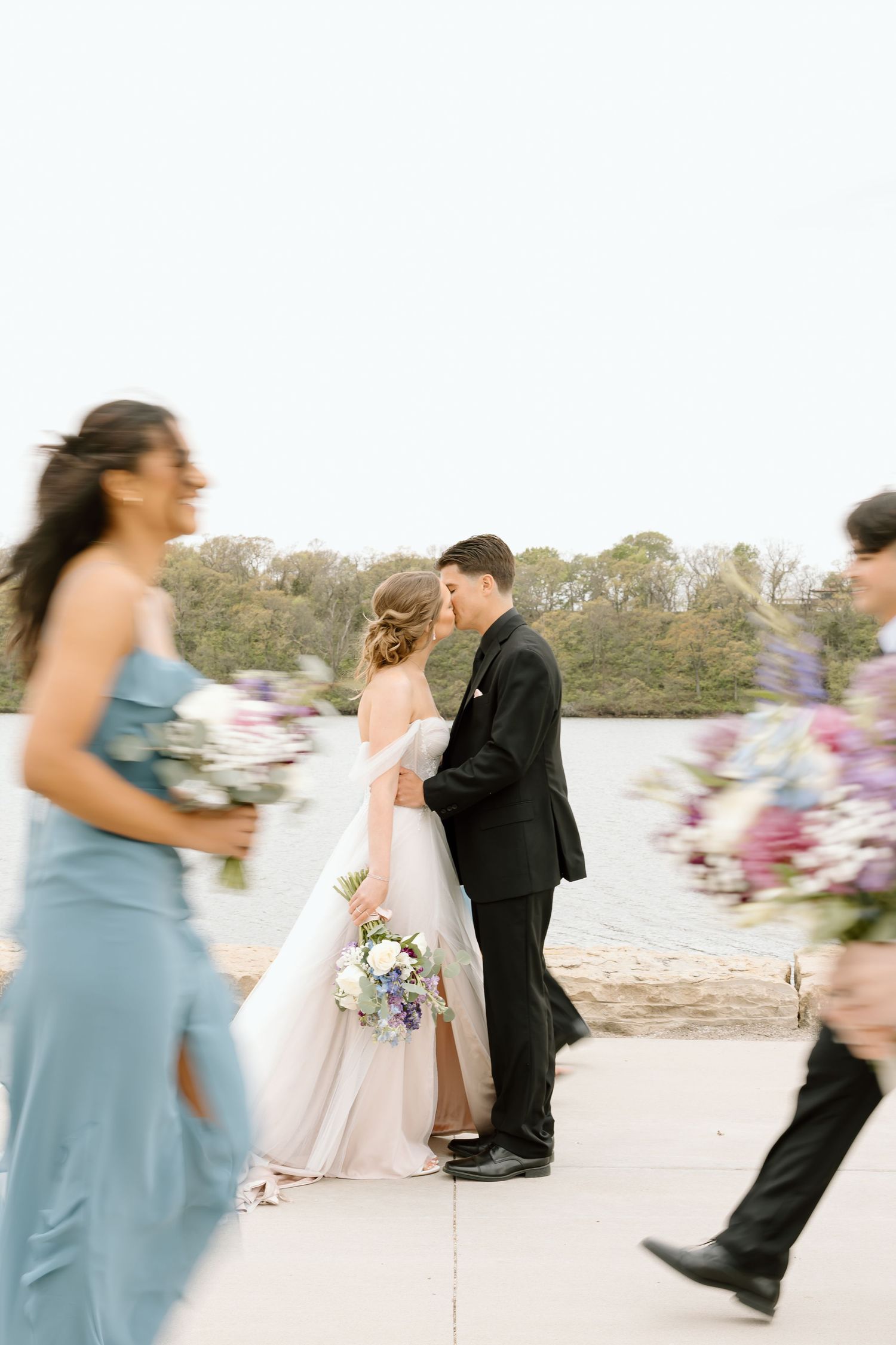 Candid wedding photo moment with bridesmaids in blue dresses moving past the couple.