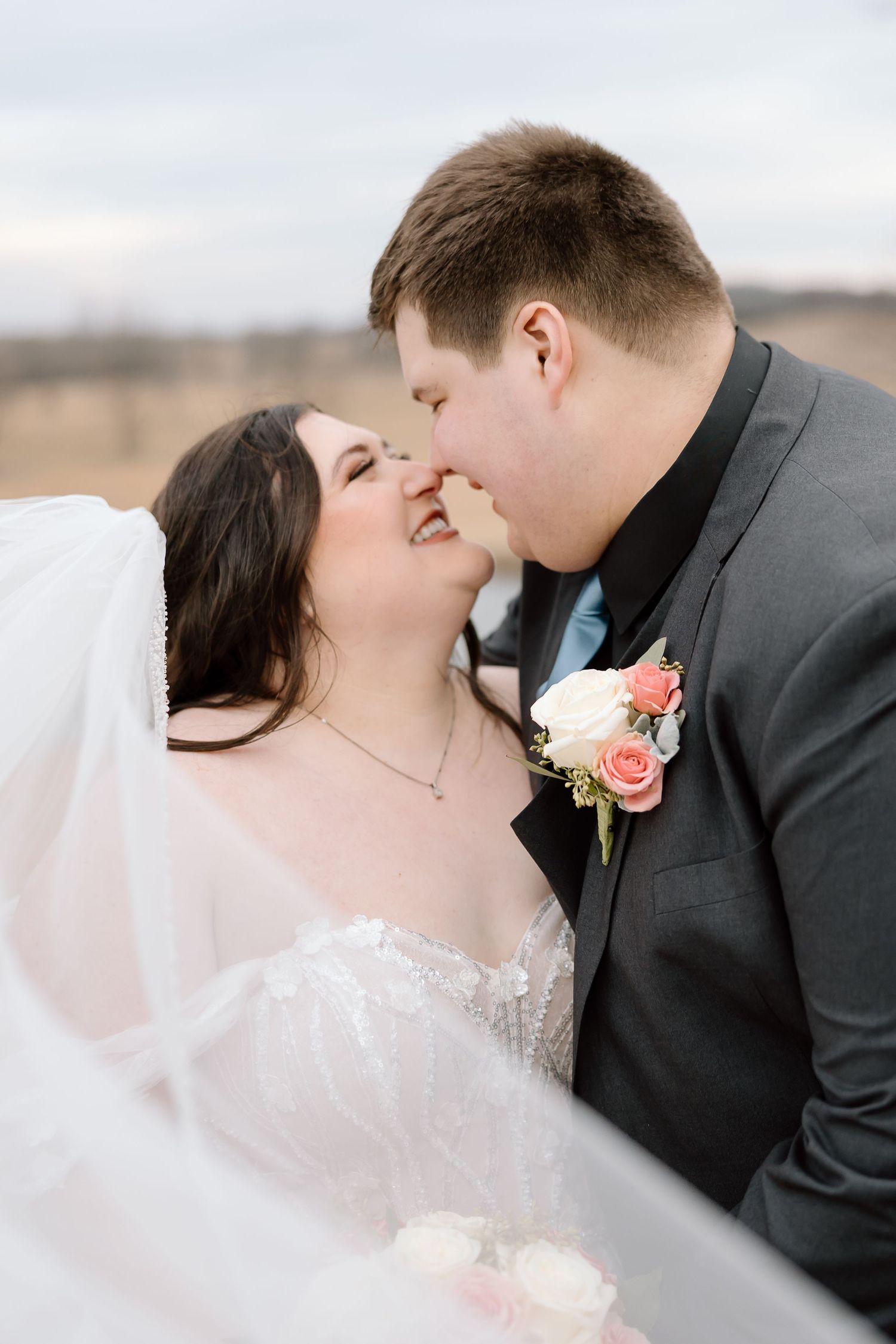 A romantic wedding moment captured outdoors with a bride in white and groom in dark suit sharing an intimate kiss.