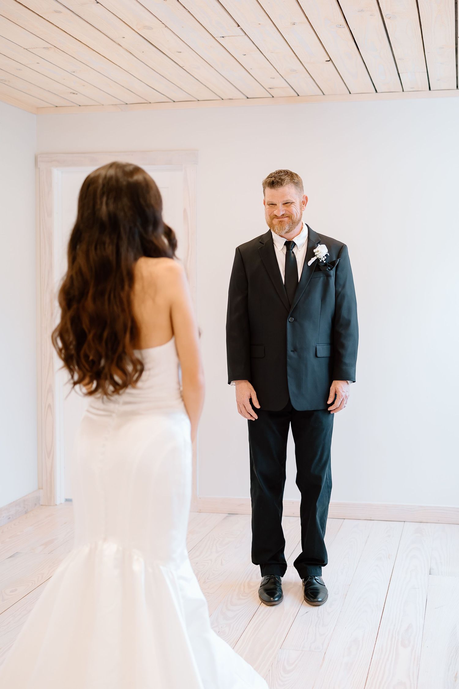 A series of wedding photos showing a first look moment between a bride in white and groom in dark suit against white walls.