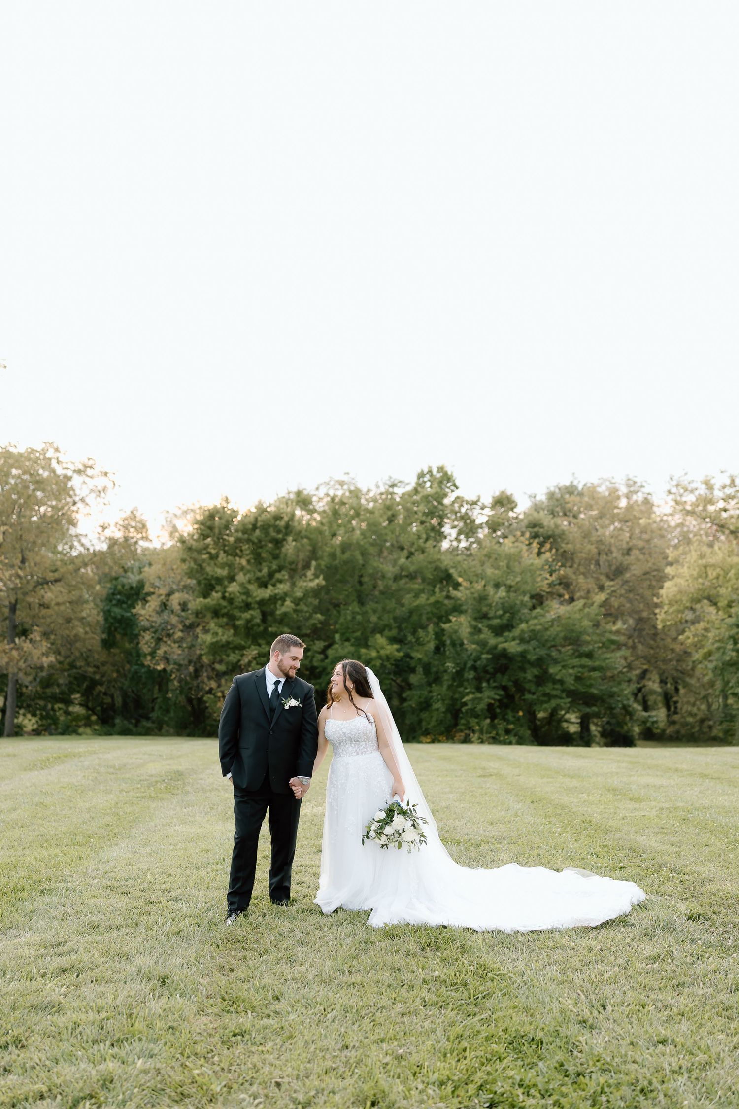 A couple in wedding attire stands together on a grassy hillside during their outdoor ceremony.