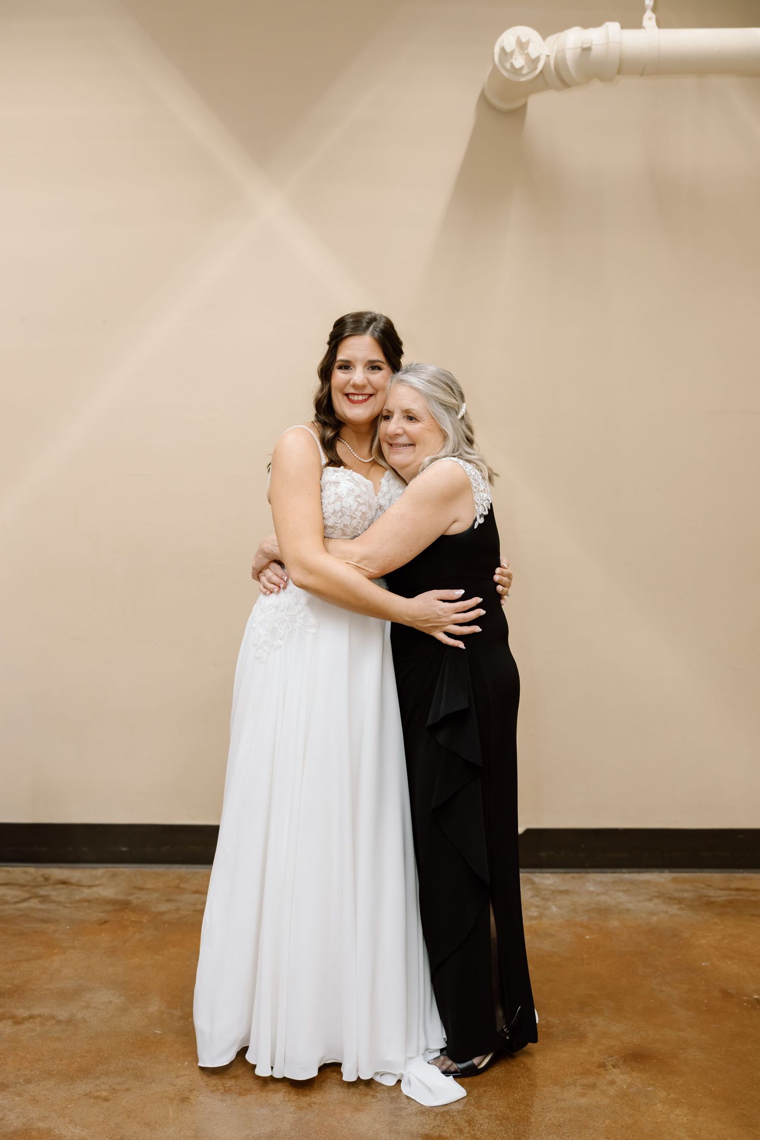 A bride in a white wedding dress and sneakers embraces an older woman wearing a formal black dress.