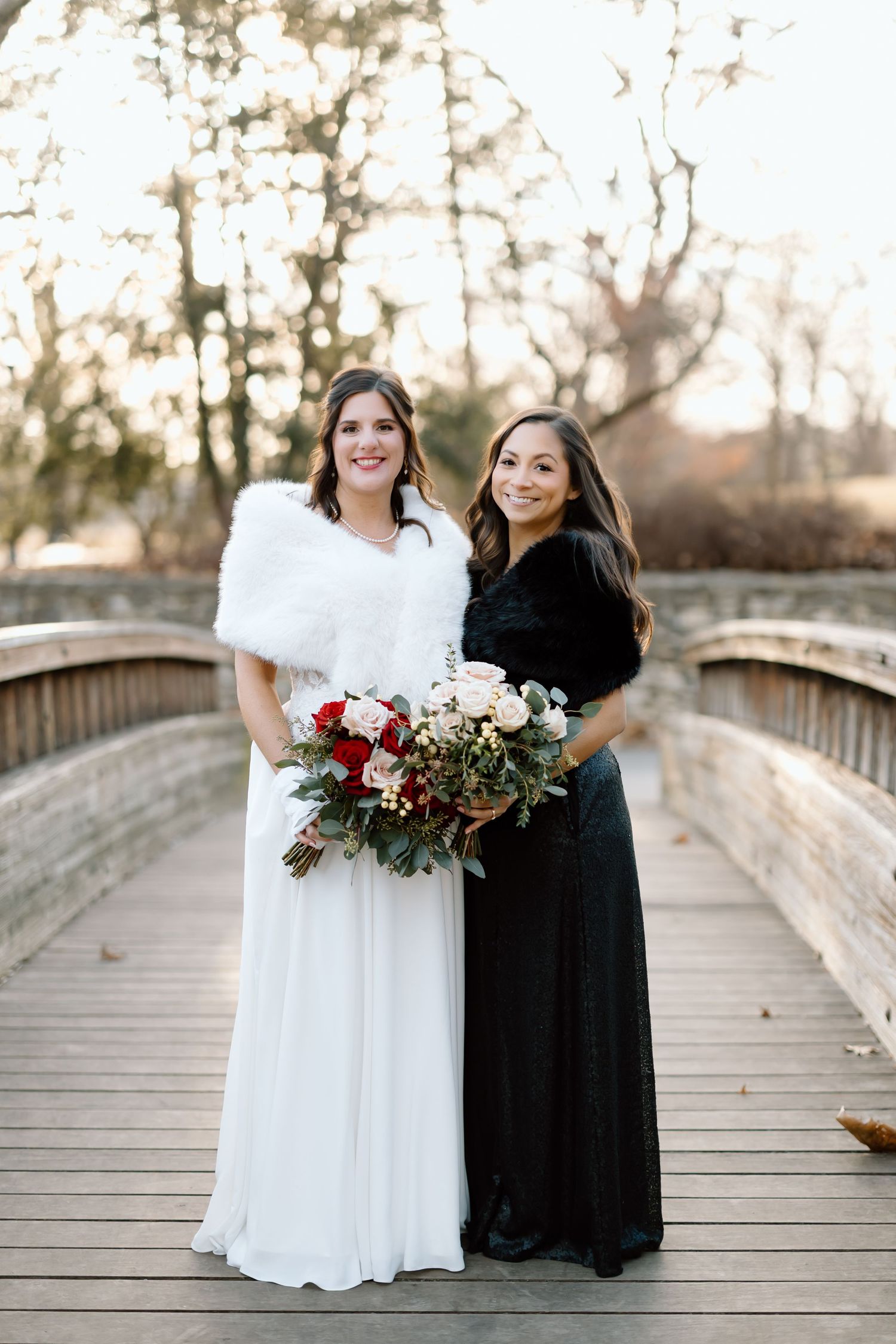 Two people in contrasting white and black dresses share joyful moments together on a wooden bridge during a photo session.