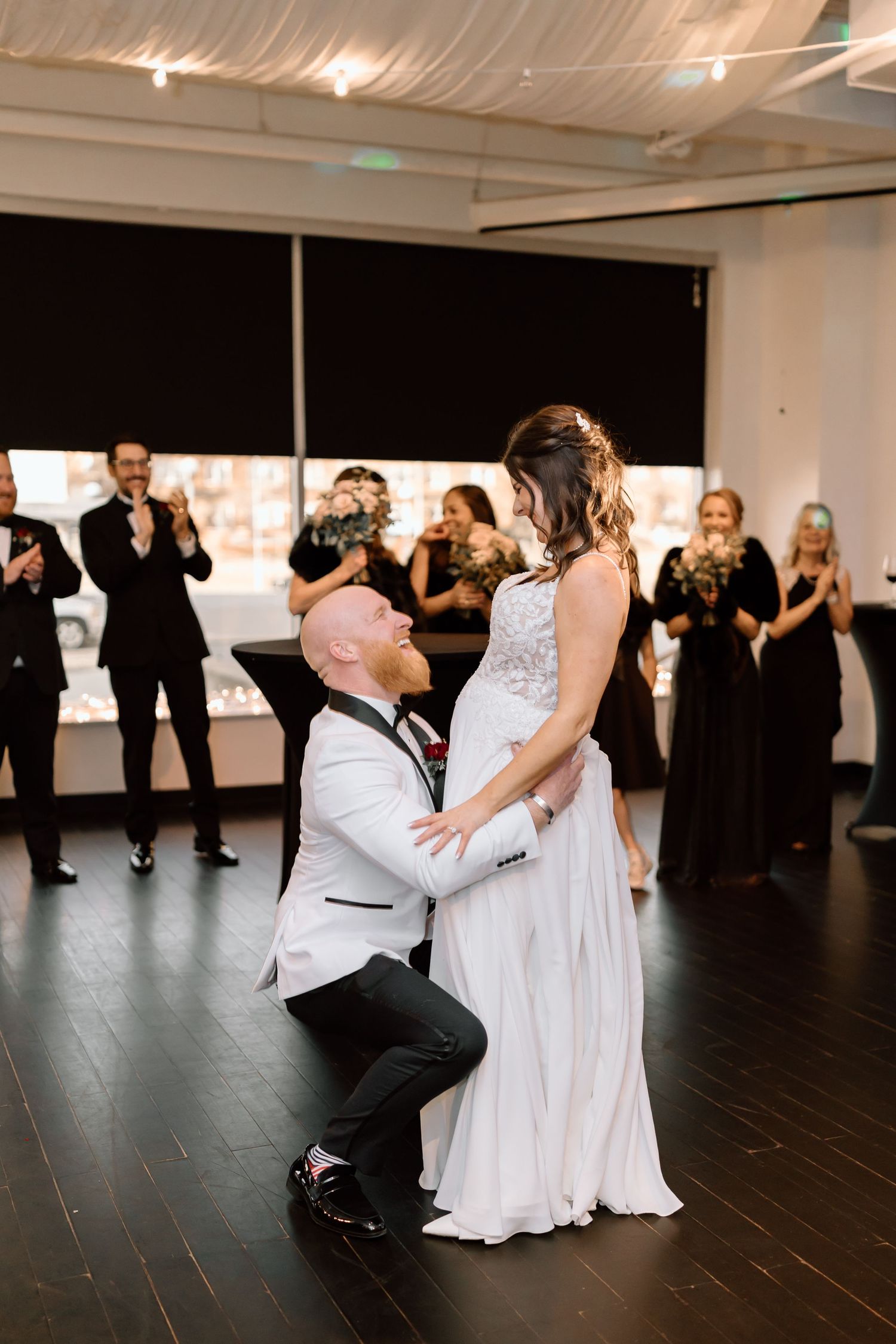 Wedding party performs choreographed dance routine in a modern studio space with dark flooring and white walls.