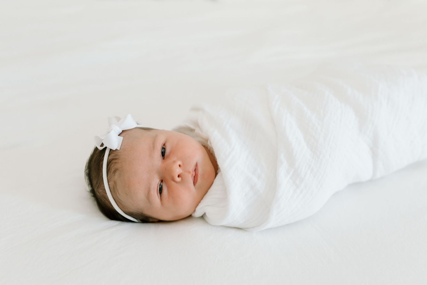 A sleeping baby wrapped in white blankets rests peacefully against a white background.
