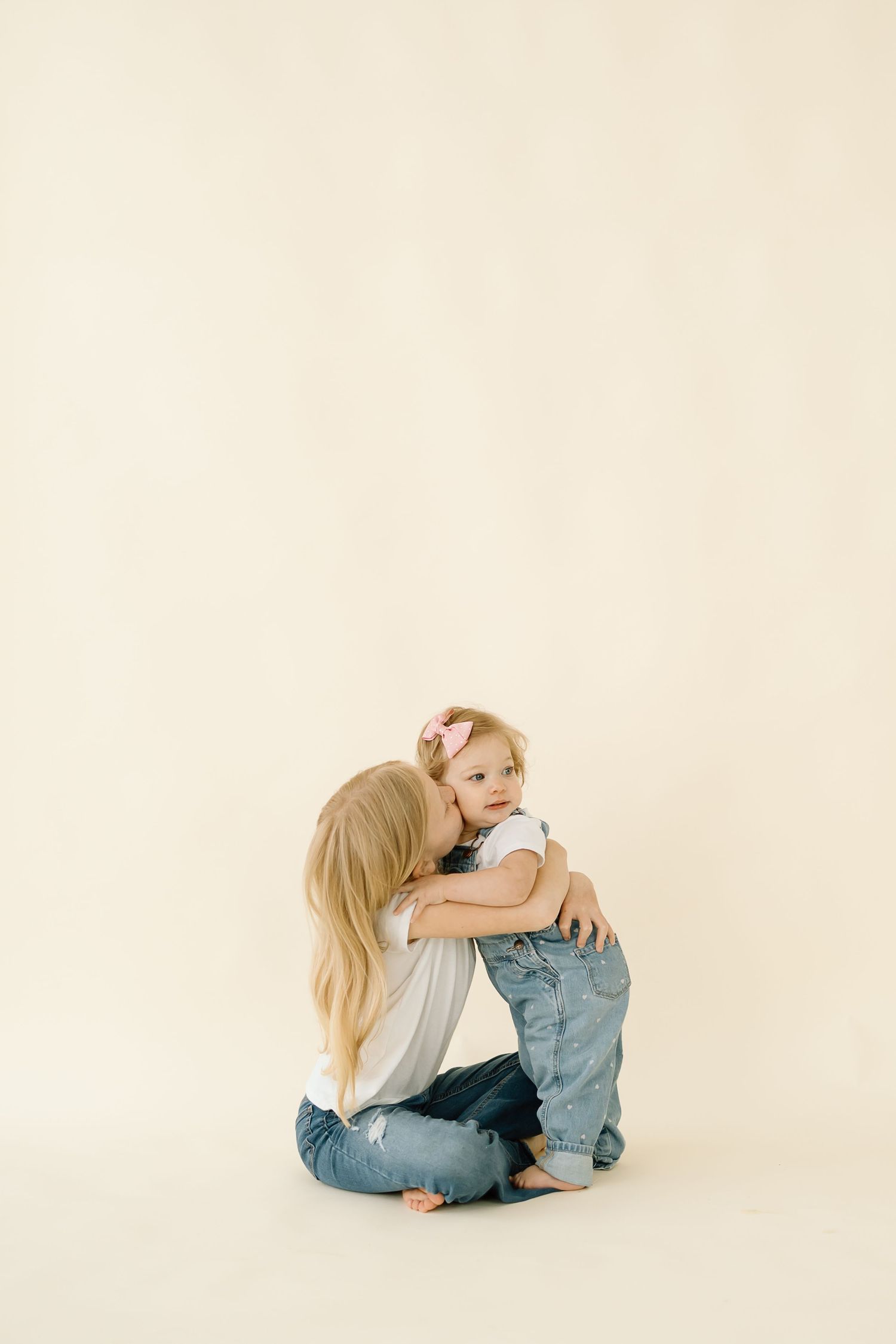 Parent and child share a tender embrace while sitting on a white floor wearing casual denim outfits.