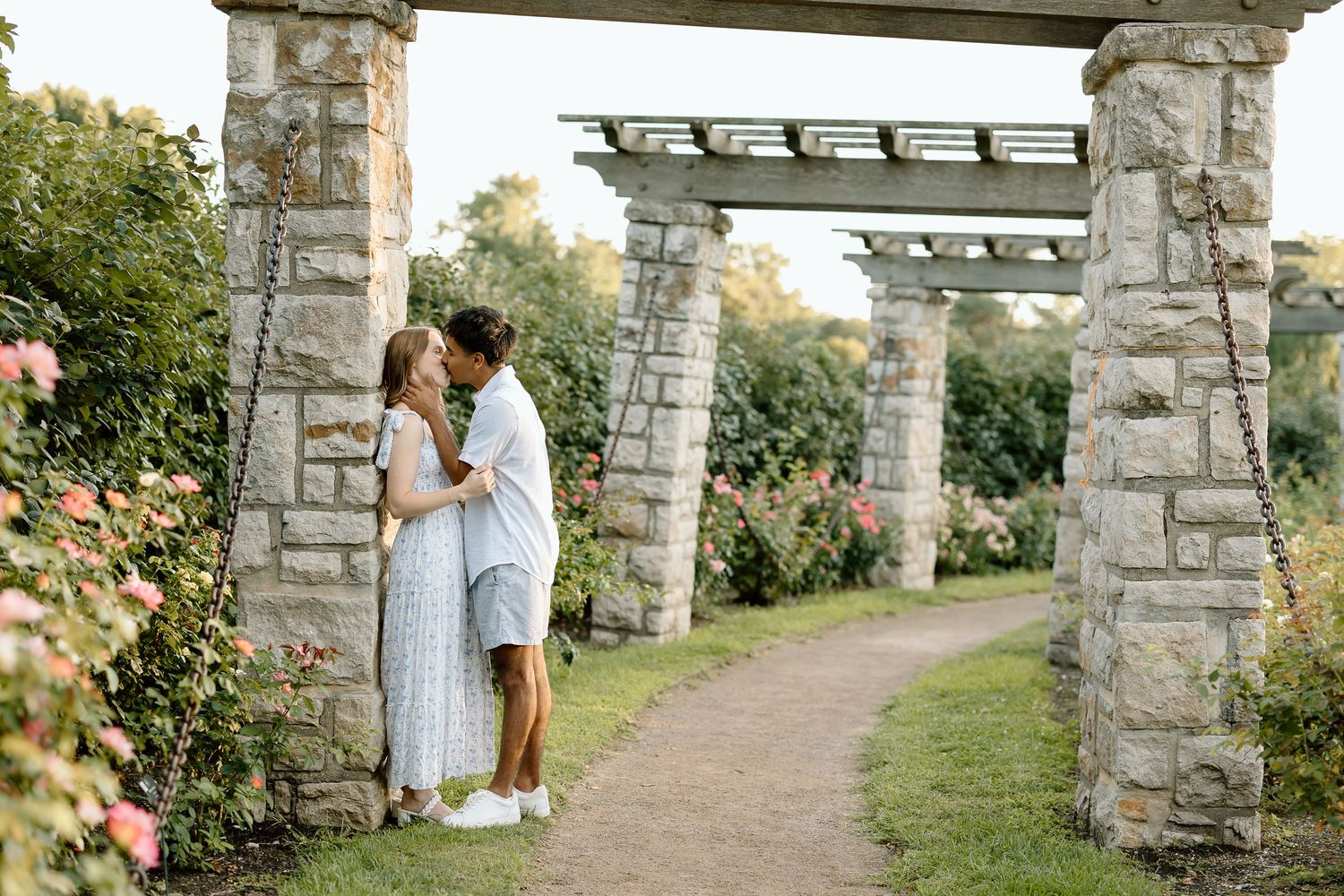 A couple shares a romantic moment under stone archways in a garden setting at sunset.