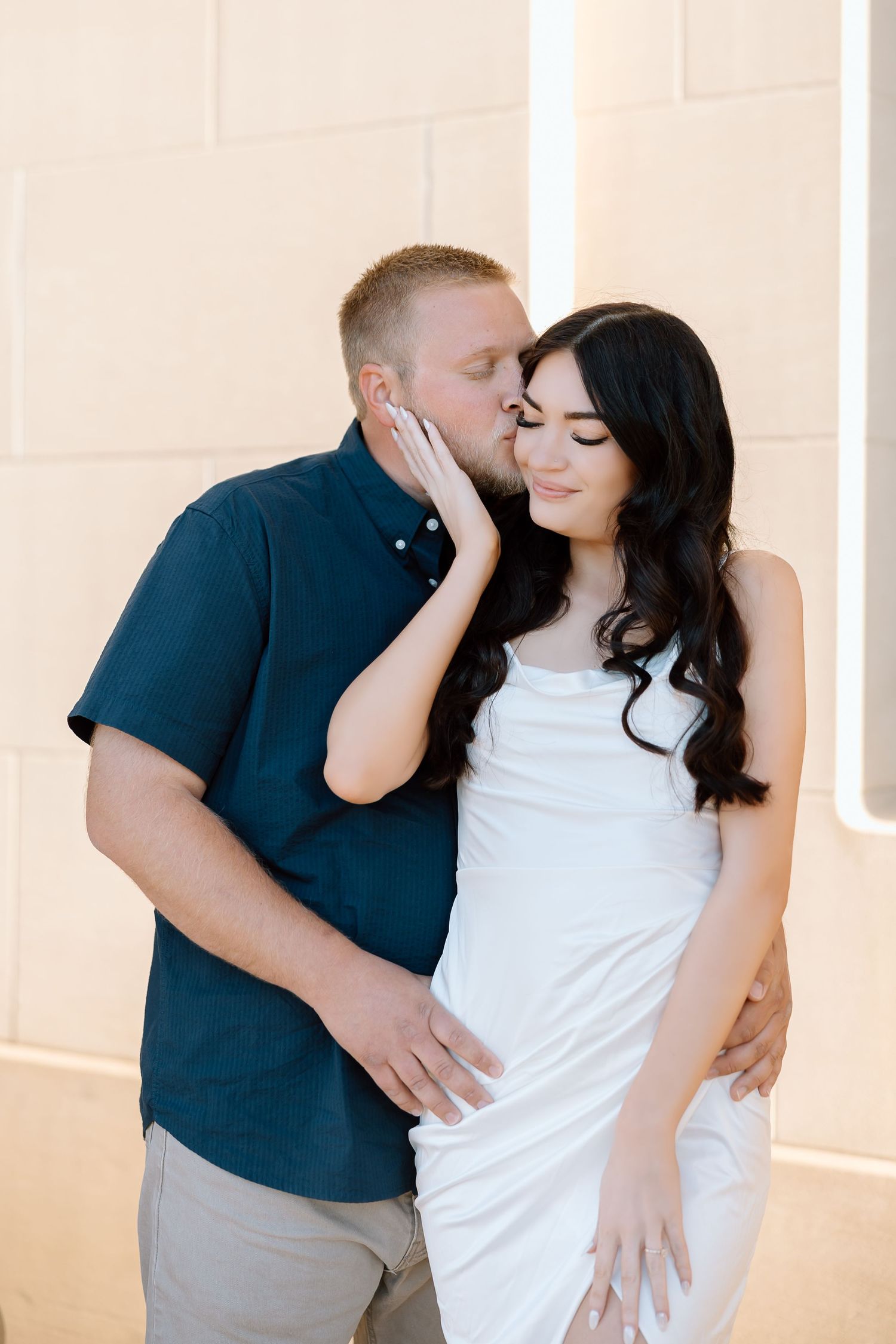 A couple in coordinated navy and white outfits share intimate moments in a bright, minimalist studio setting.