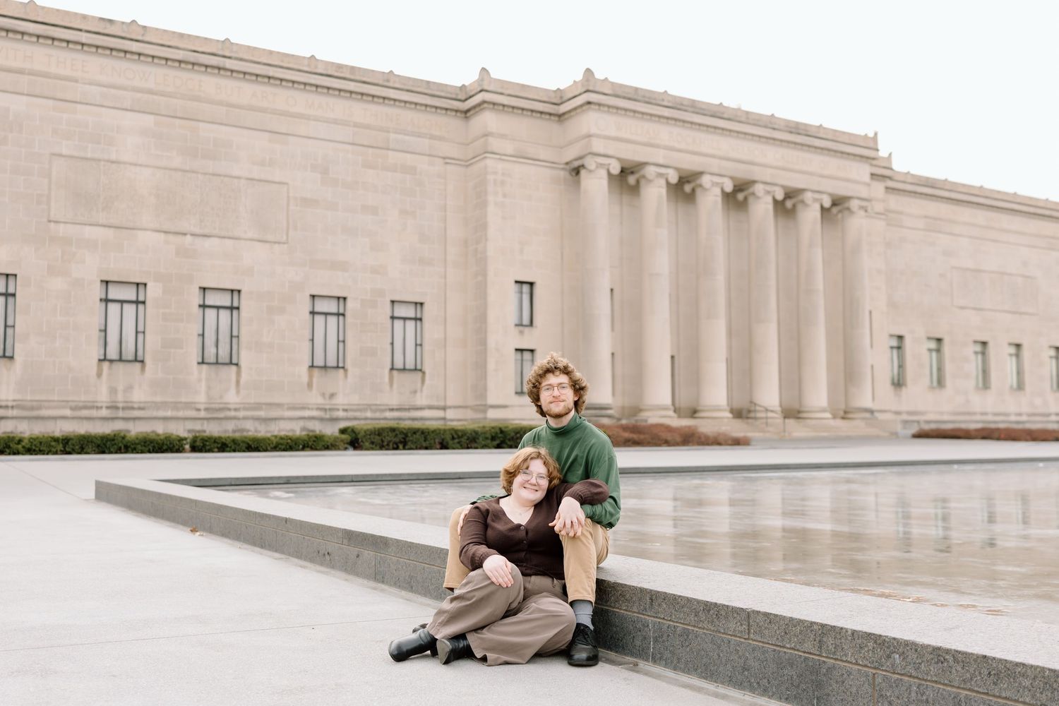 Couple poses dramatically on stone steps of classical building exterior.