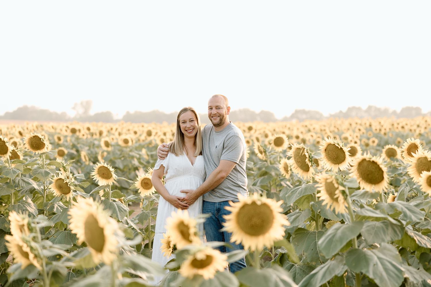 A couple stands together in a golden sunflower field at sunset creating a romantic silhouette against the warm sky.