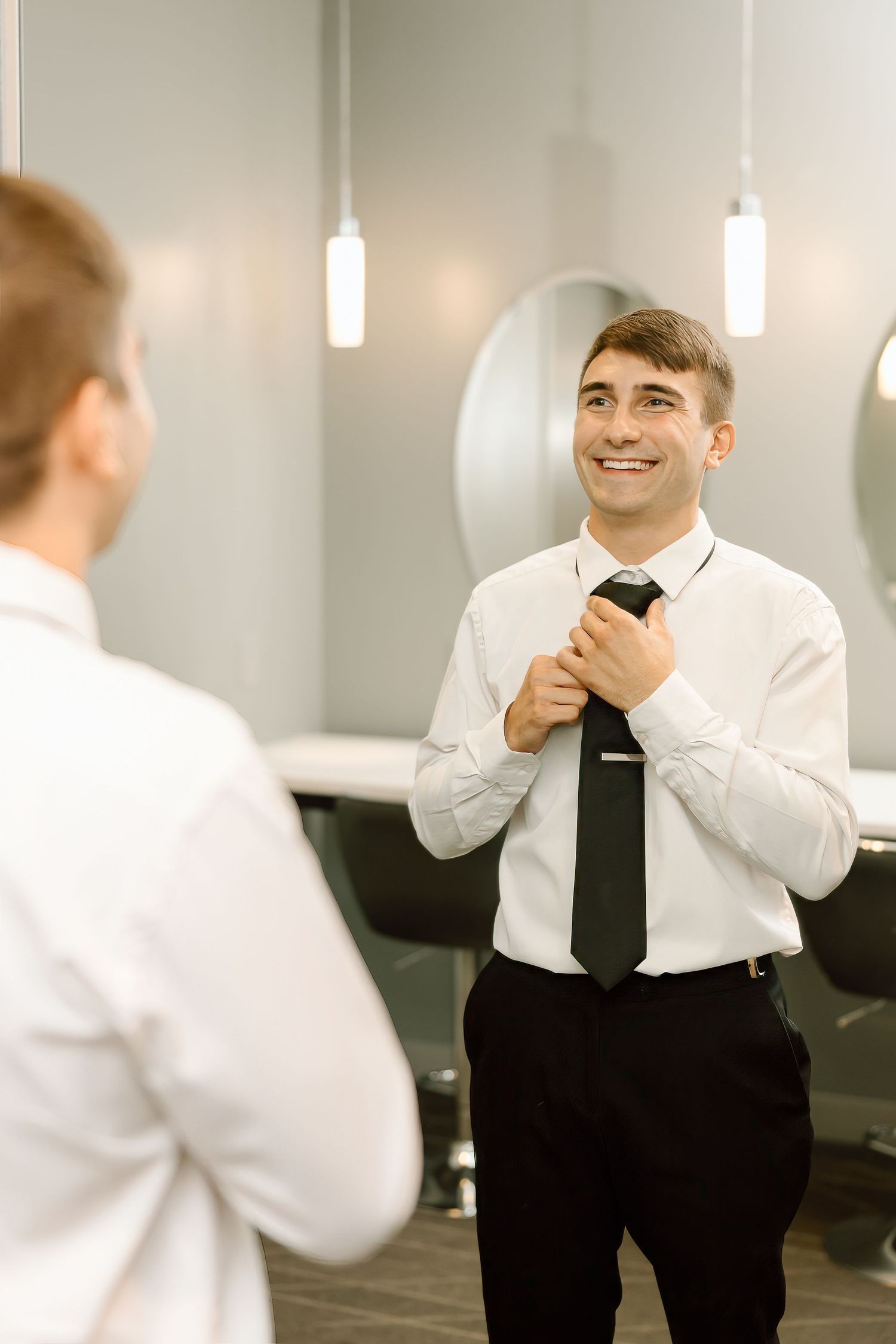 Office worker in white dress shirt and black tie adjusts his necktie while standing in a bright corridor.