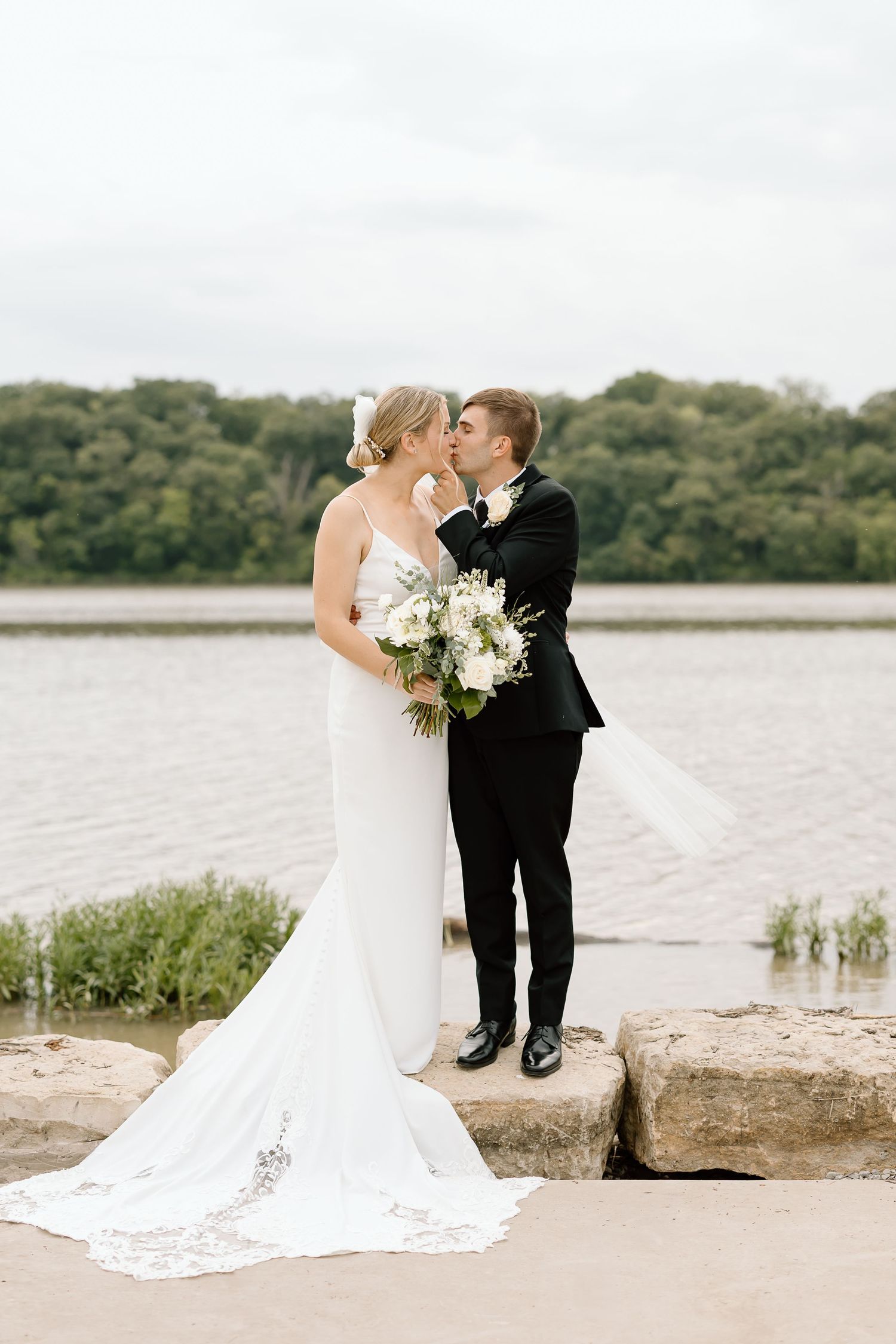 A romantic newlywed couple shares an intimate moment by a serene lake on their wedding day.