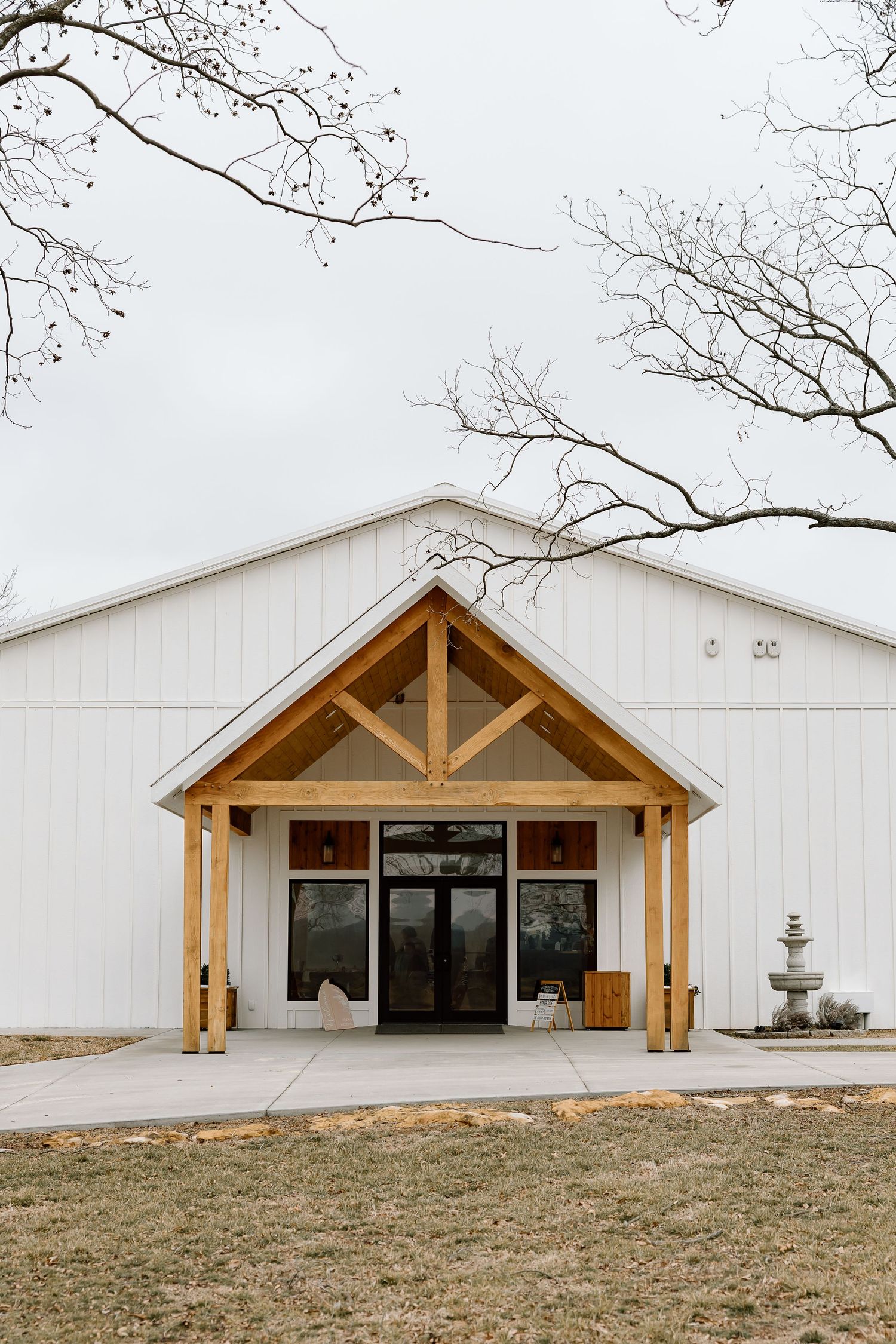 Modern white barn-style wedding venue with wooden timber frame entrance and large glass doors in rustic outdoor setting.