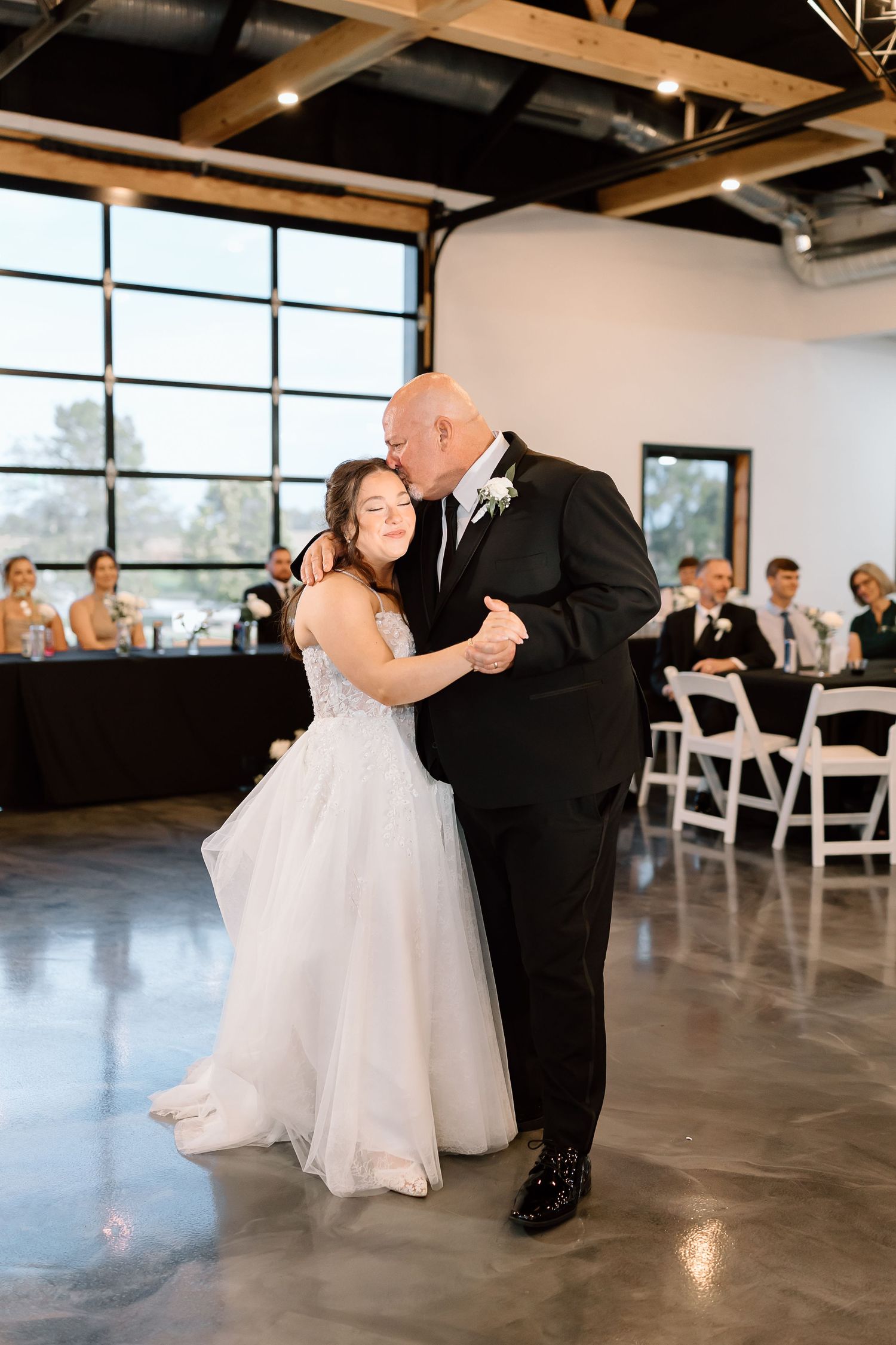 A couple shares a romantic dance together at their wedding reception in an industrial-style venue with exposed beams.