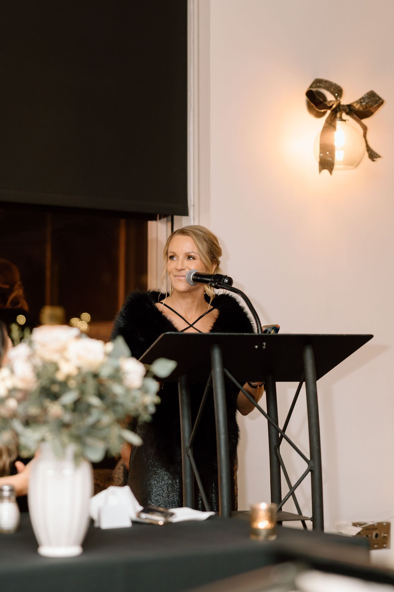 A series of moody candlelit reception tables with black chairs and white floral centerpieces at an elegant event venue.