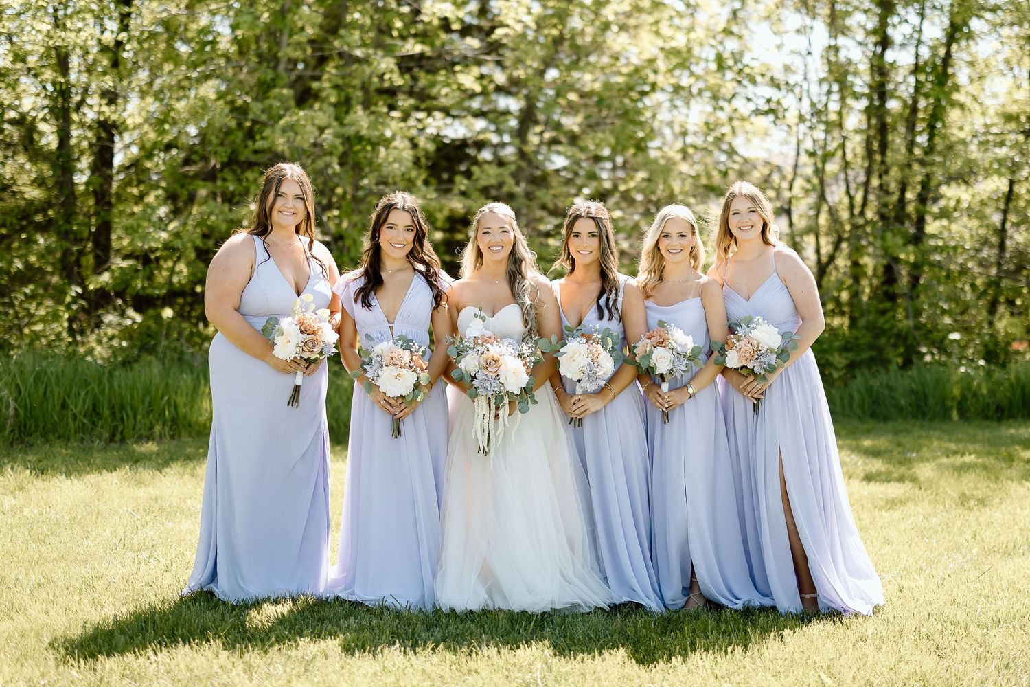 Bridal party in flowing light blue dresses posing together in sunny garden setting.