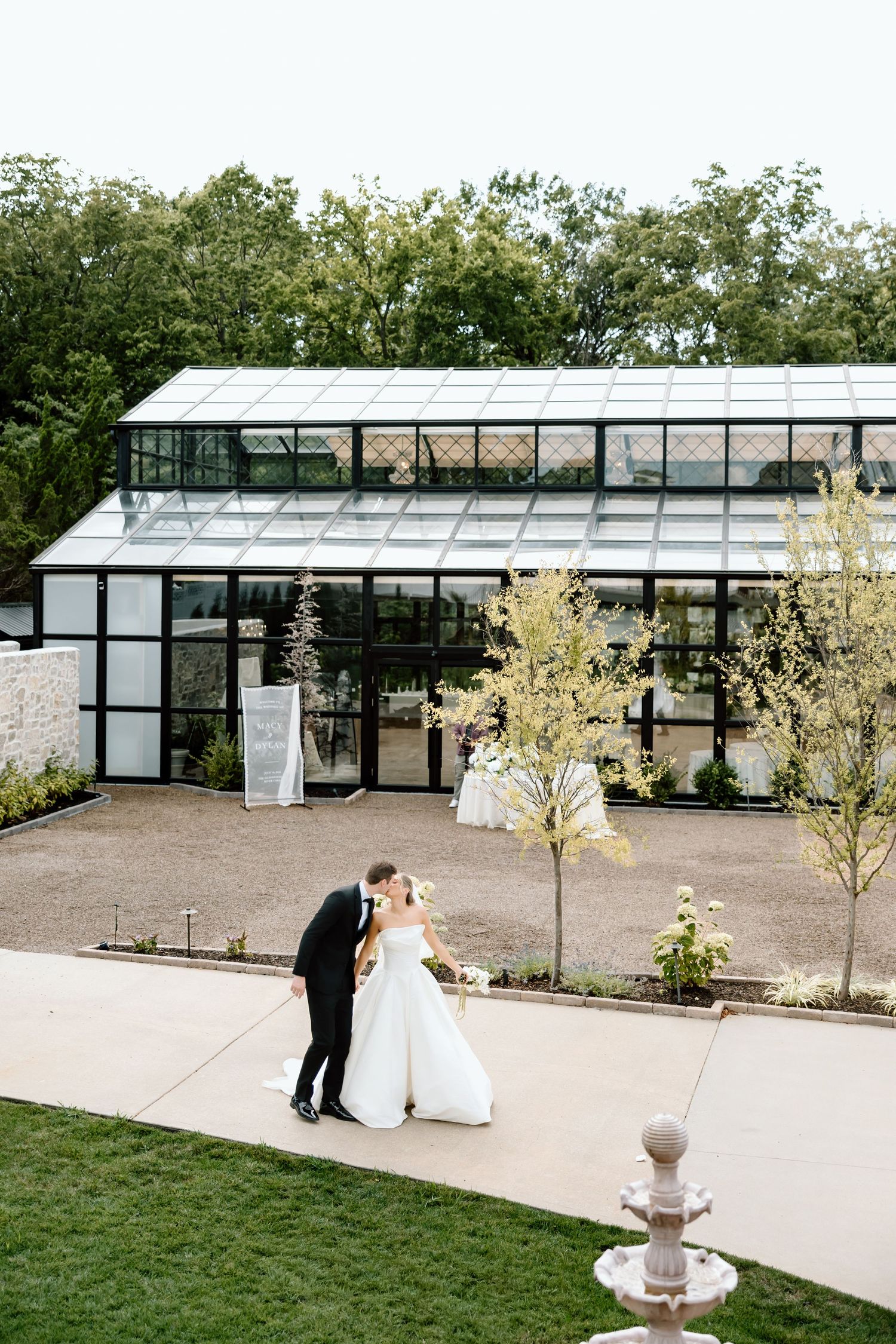 Bride and groom share a romantic moment outside an elegant glass greenhouse wedding venue surrounded by lush greenery.