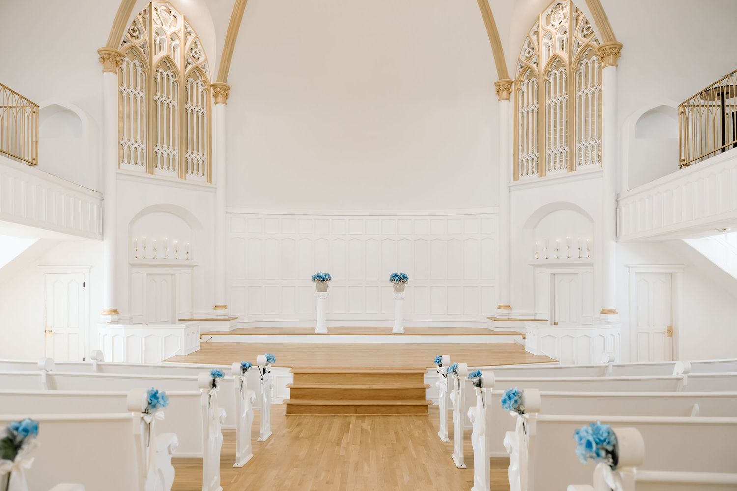 Elegant white church wedding venue with blue floral arrangements on pews and altar, featuring gold organ pipes and high ceilings.