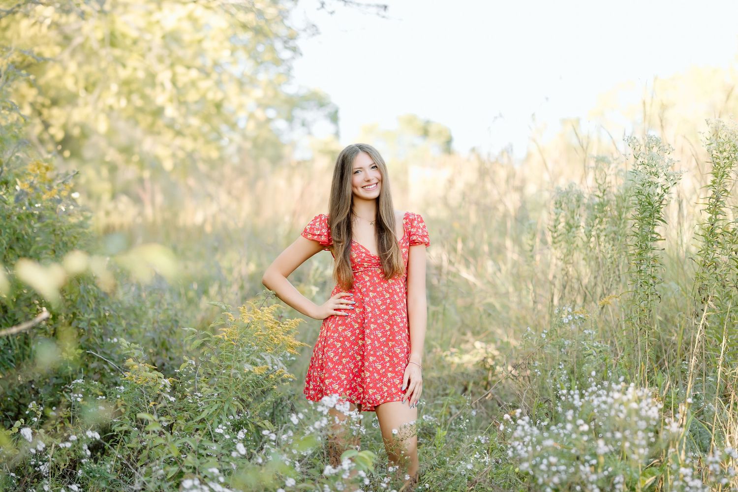 A person in a red dress twirls joyfully in a sunlit meadow filled with white wildflowers at golden hour.