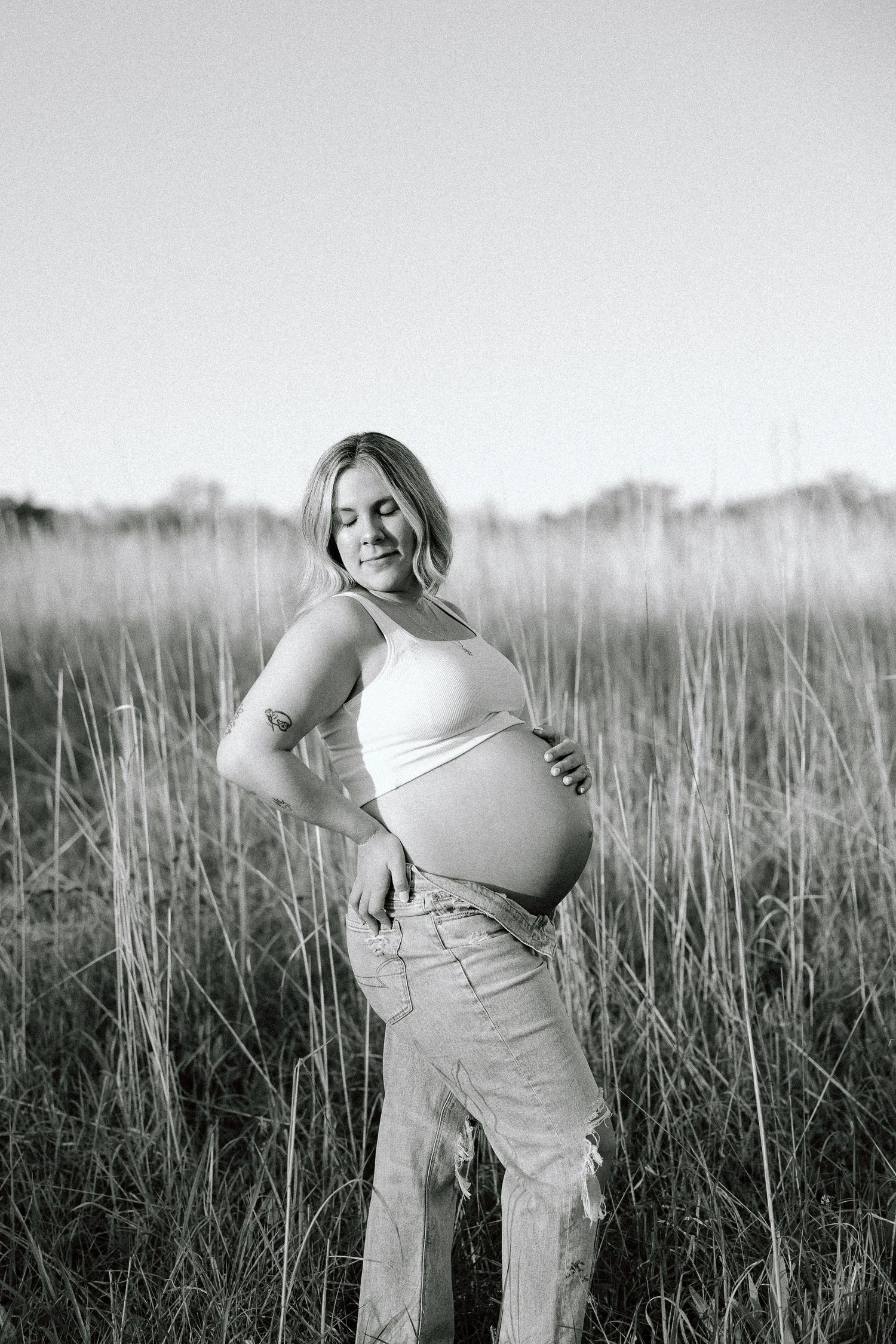Black and white artistic portrait series of a woman in a dress posing expressively in a grassy field at sunset.