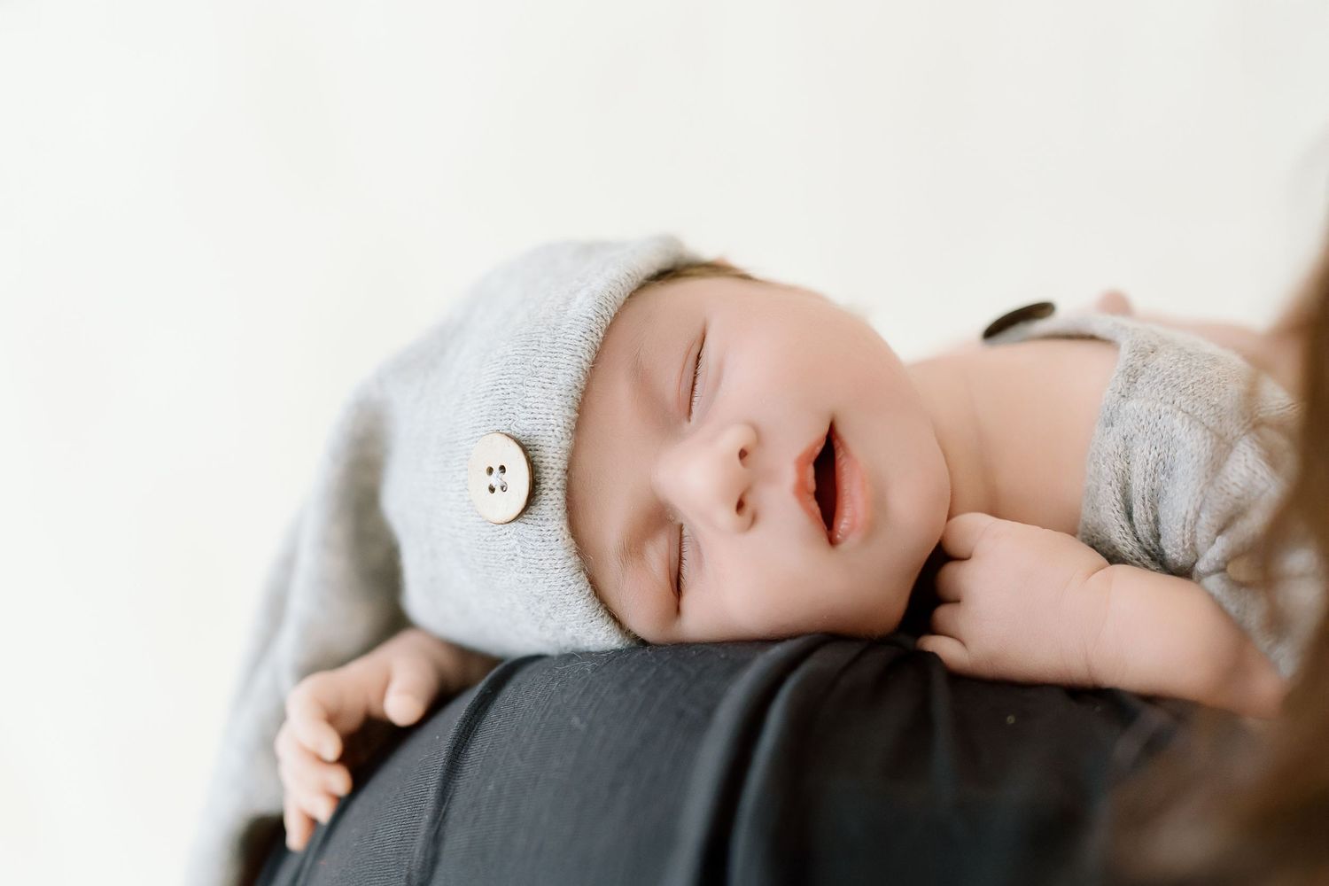 A sleeping baby wearing a gray onesie lies peacefully on white bedding.