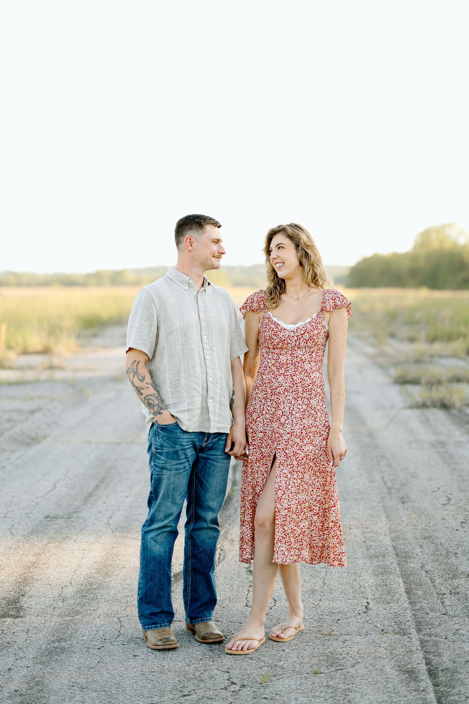 A couple in casual attire shares tender moments on a dirt road at sunset.