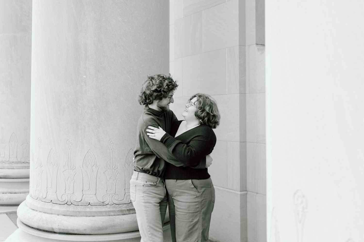 Two figures walk past white classical columns in a minimalist architectural scene.