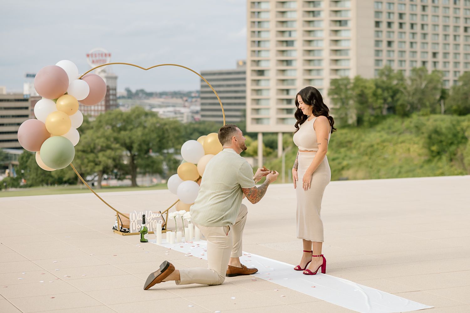 Romantic rooftop proposal scene with pastel balloons and Kansas City skyline.