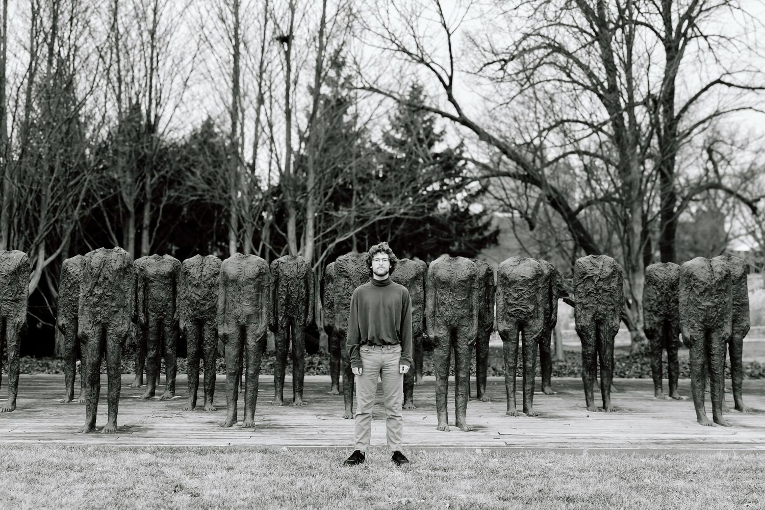 A black and white panoramic photograph shows a winter landscape with bare trees in a park or public space.