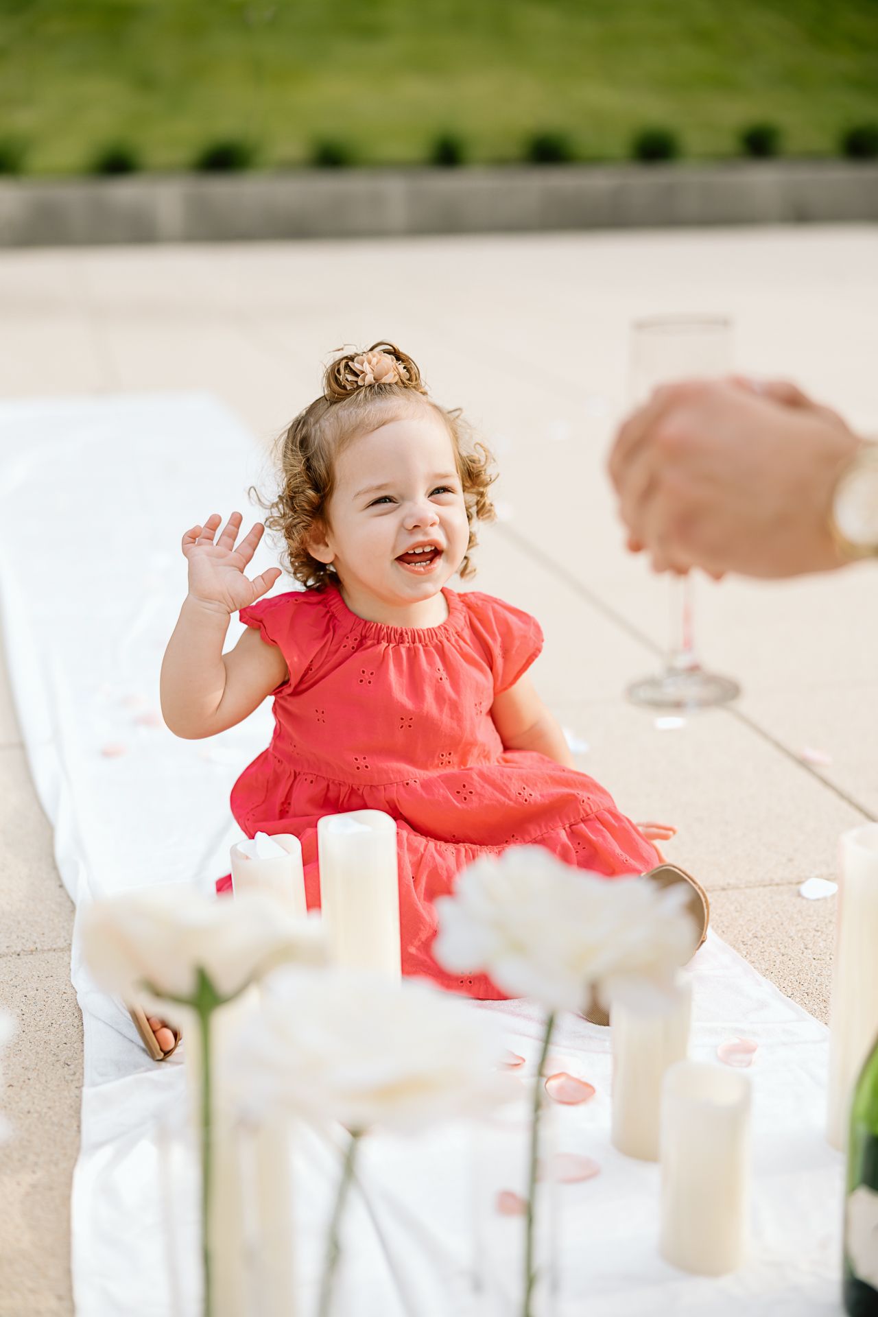 A child in a bright coral dress laughs joyfully at a white-decorated celebration table.