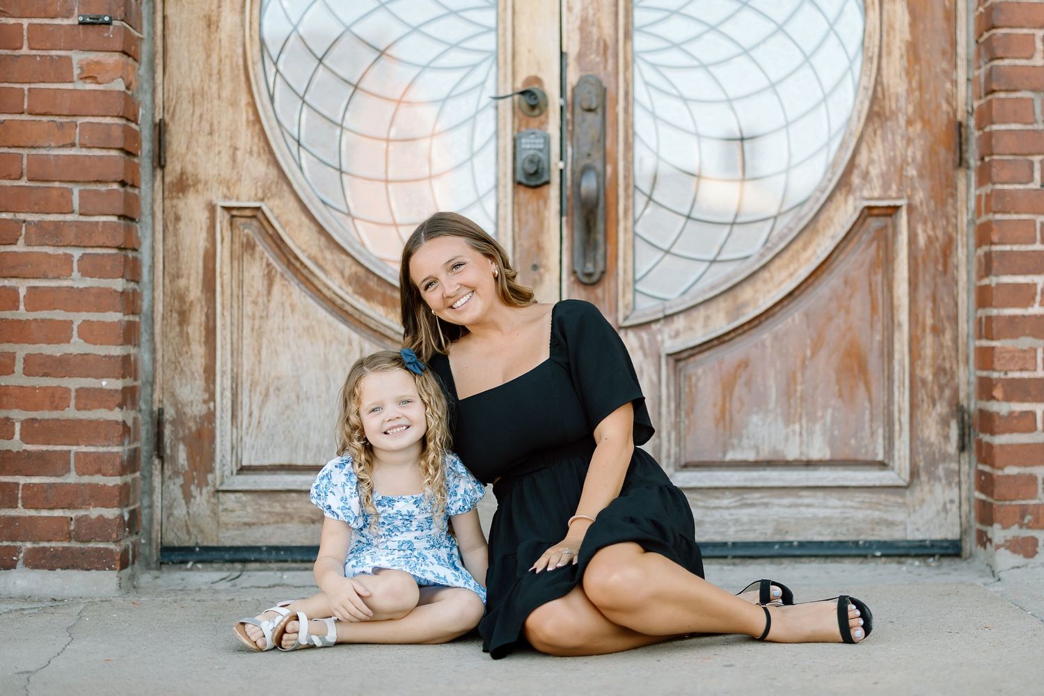 Two people in coordinating black and blue outfits pose together in front of a vintage wooden door with circular windows.