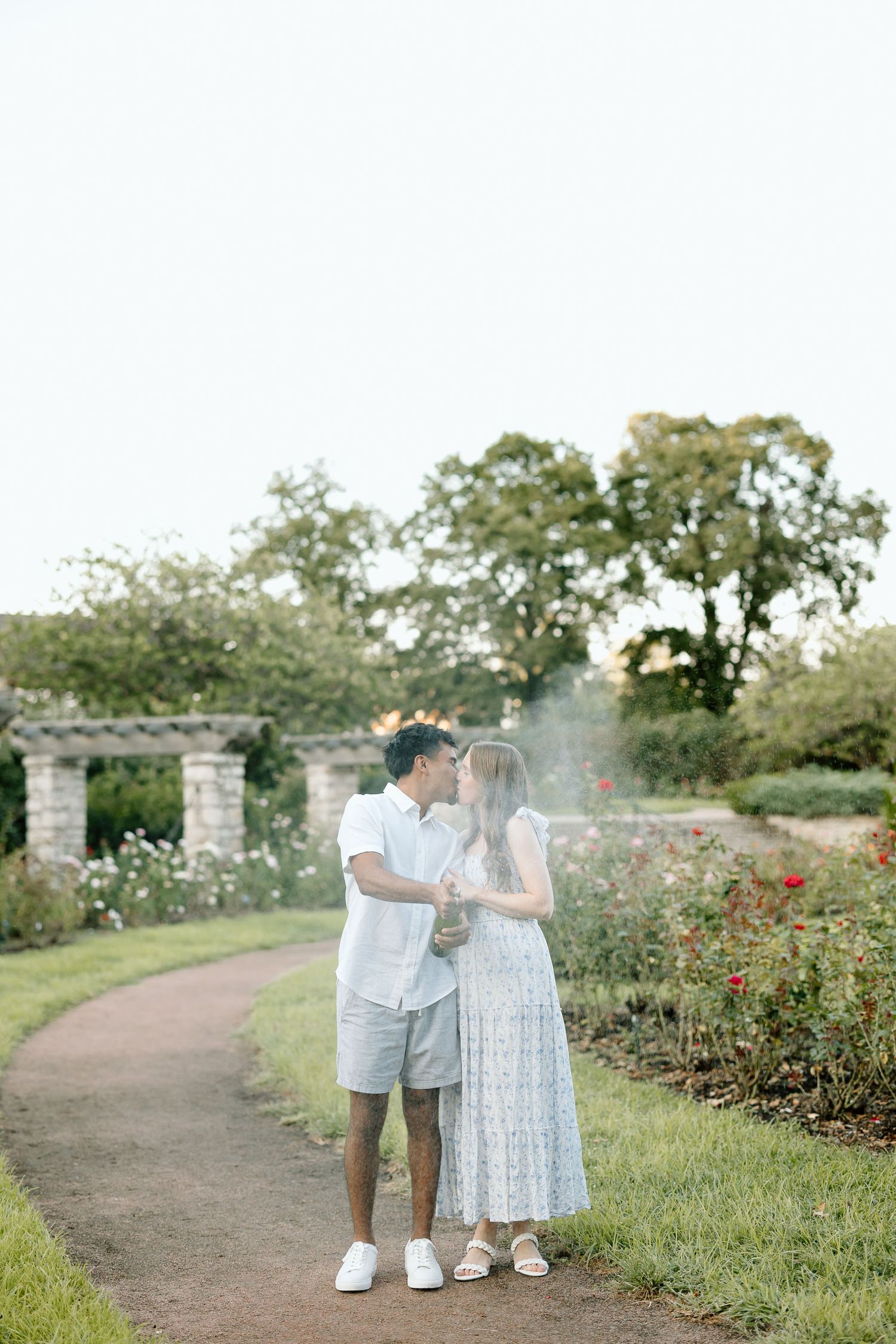 Romantic couple shares tender moments in a scenic garden path lined with blooming roses on a summer afternoon.