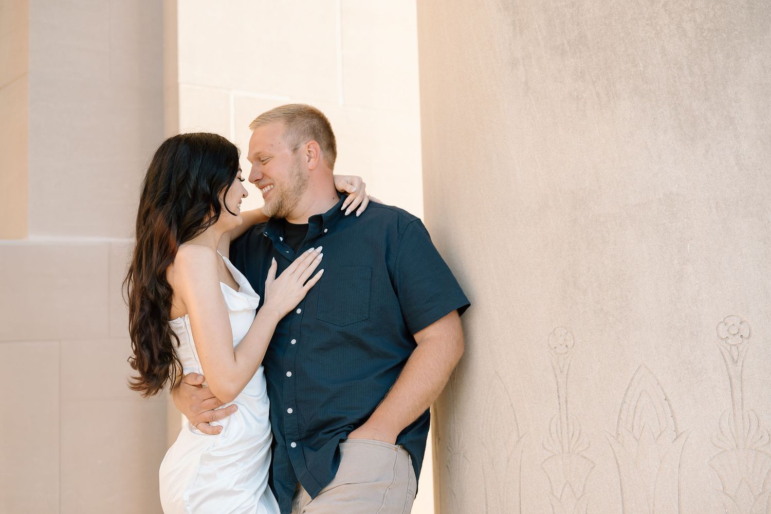 A romantic couple embraces and kisses in front of a light colored wall in a series of intimate photos.