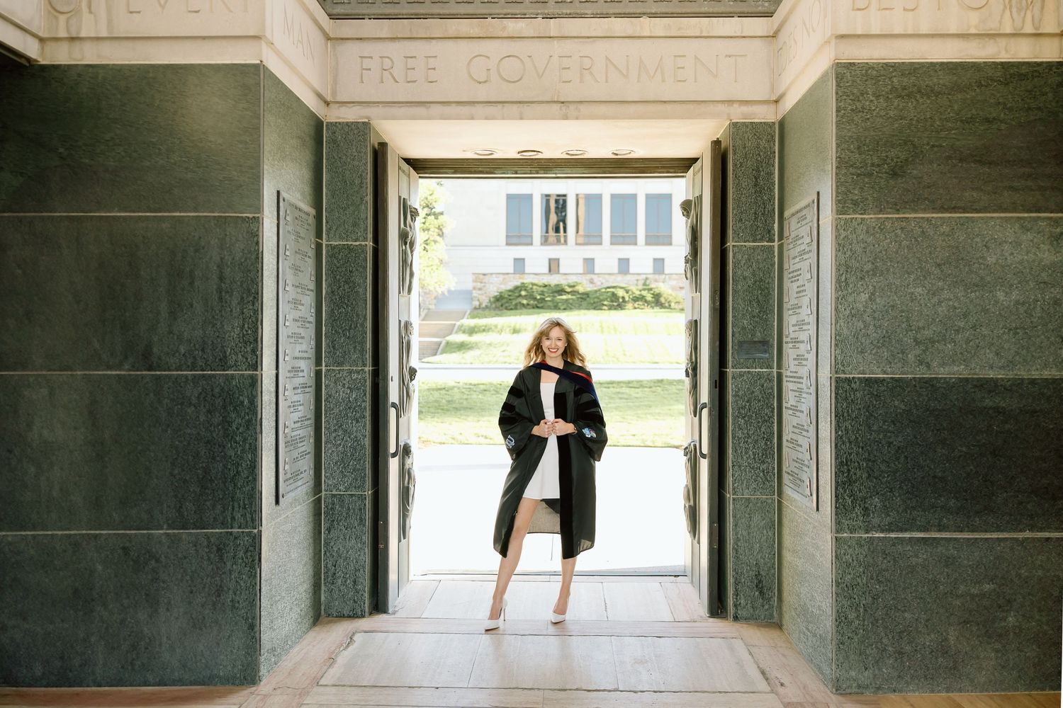 A person in a black coat and heels stands confidently in a grand marble doorway entrance.