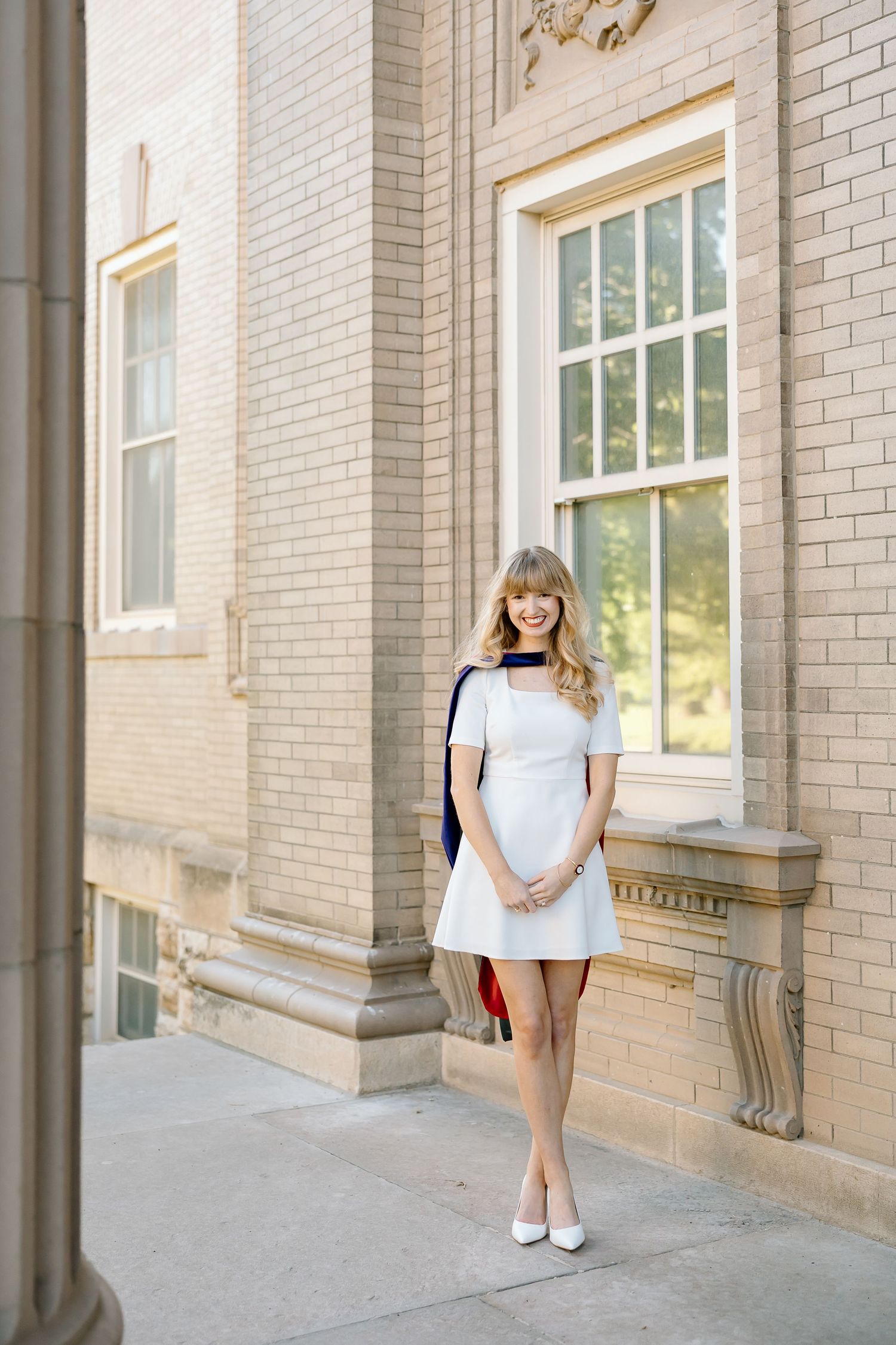 A graduate in a light blue dress stands in front of a brick building with white columns and windows.