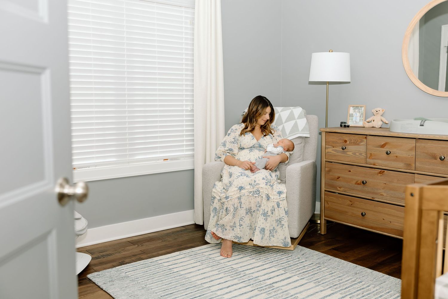 A bright nursery room features white walls, wooden furniture, and floral decor with natural lighting from windows.