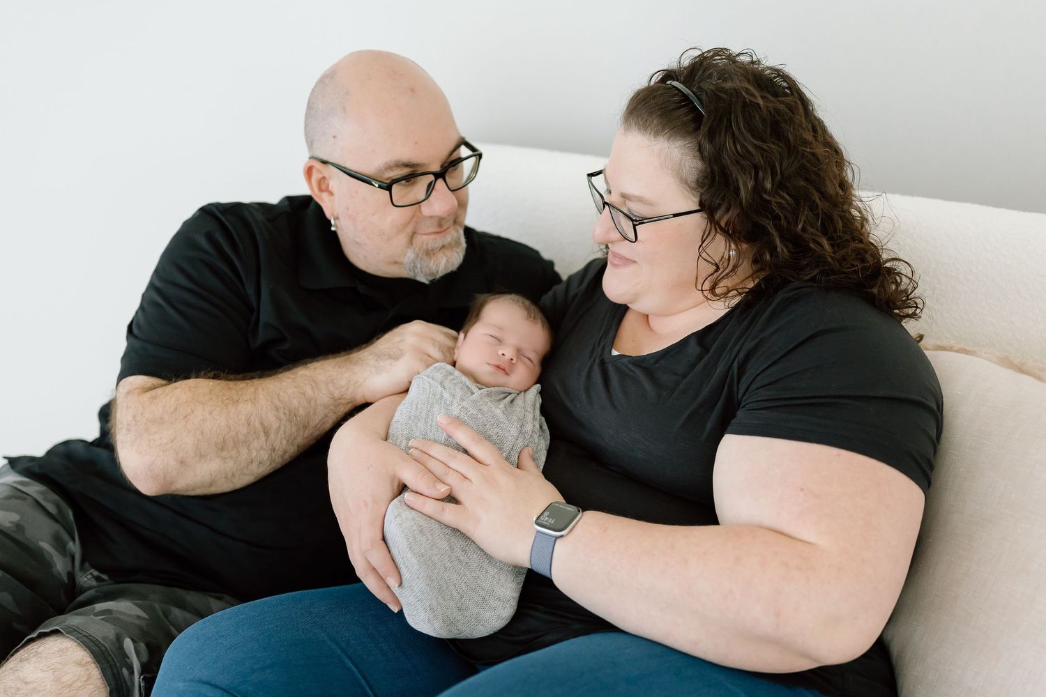 A series of five intimate black and white photographs showing tender moments between parent and newborn on a couch.