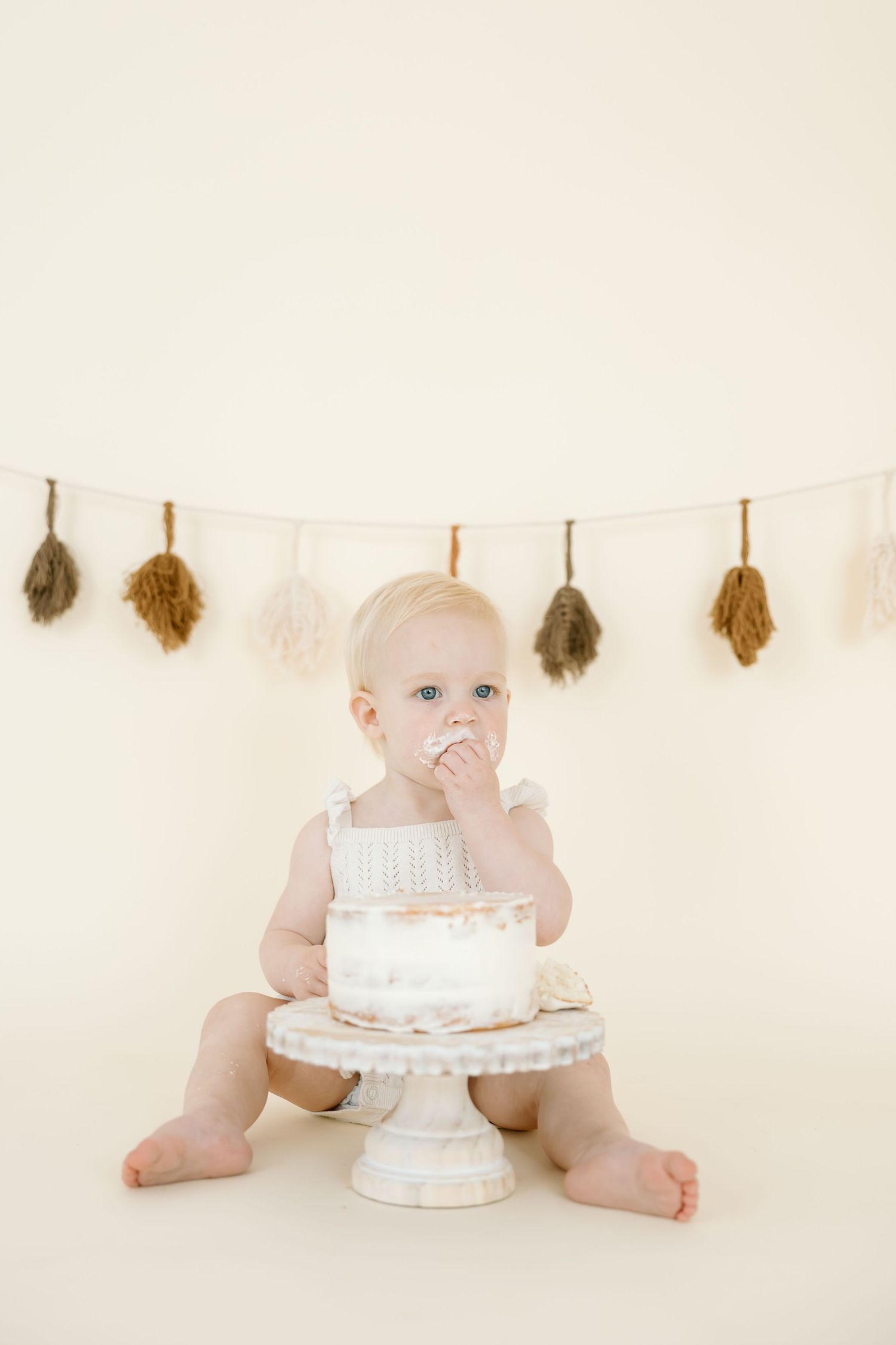 A series of three photos showing a baby in white with a cake on a white pedestal against a neutral background.