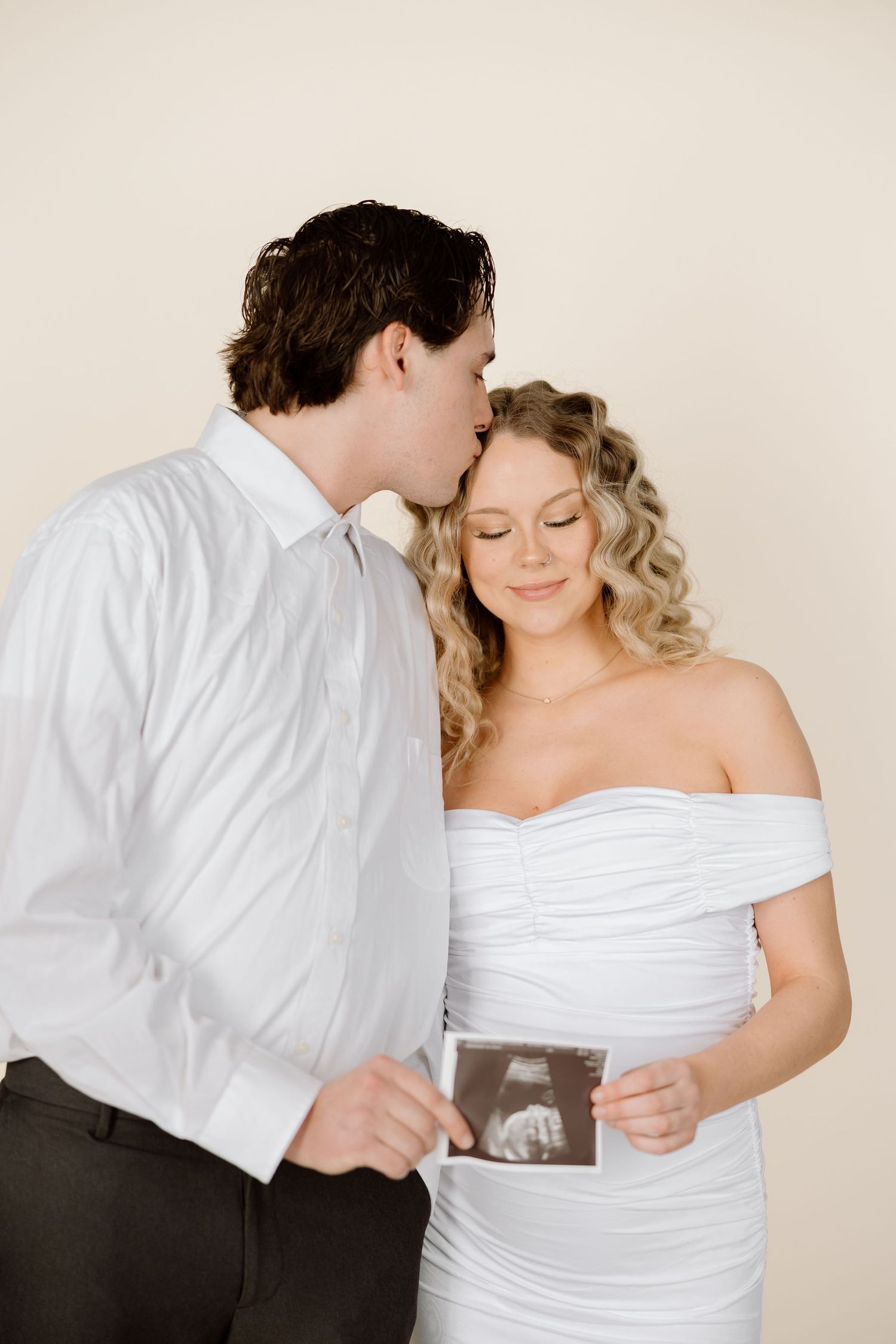 A romantic pregnancy announcement photo shows a couple embracing while displaying an ultrasound image.