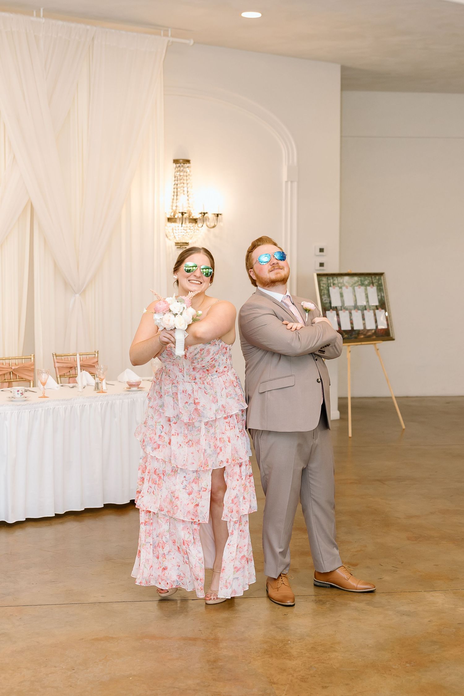 Wedding guests strike playful poses wearing fun sunglasses at a reception with white decor and champagne table.