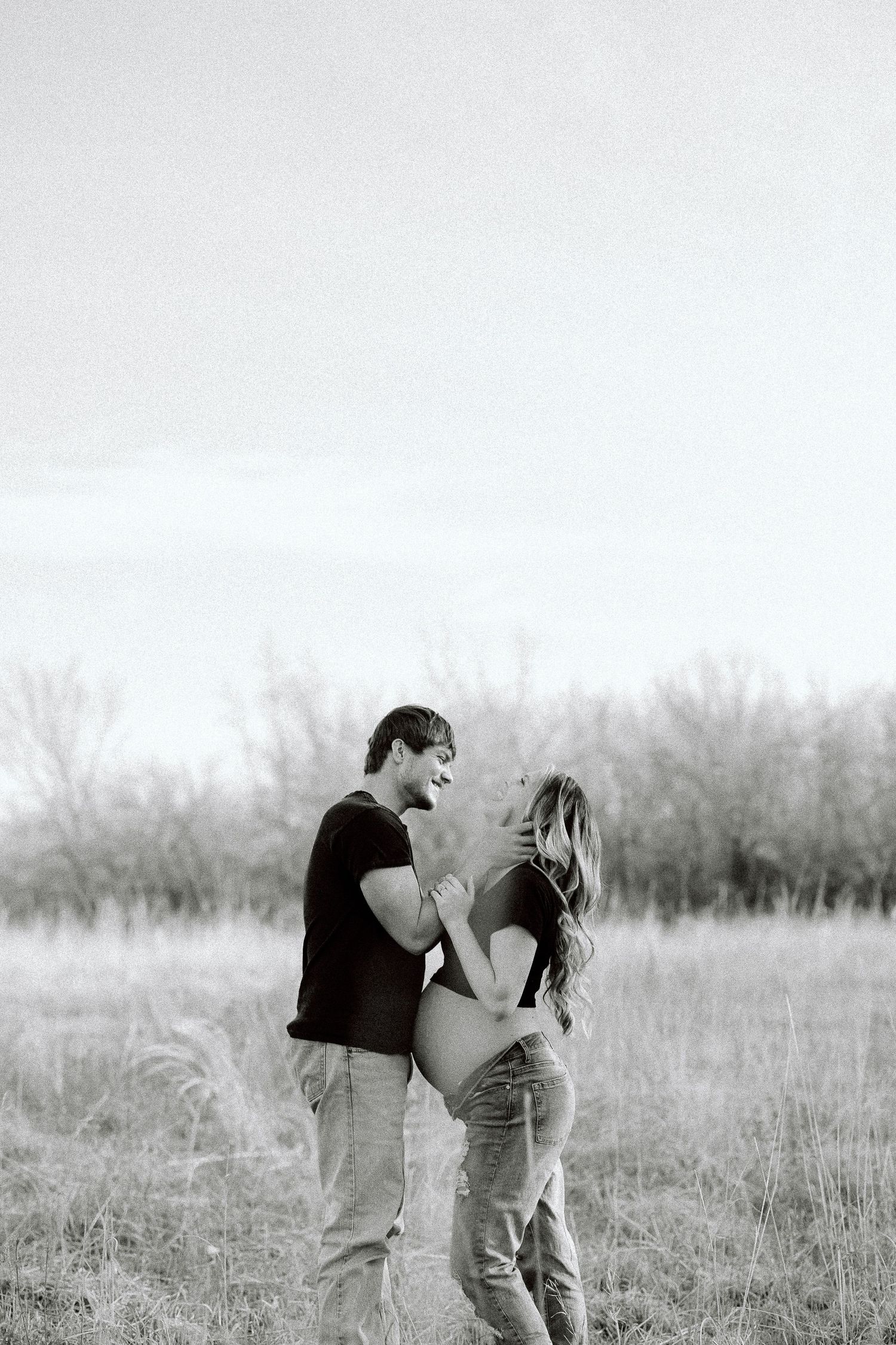 A couple embraces in a romantic moment while standing in a misty field of tall grass.