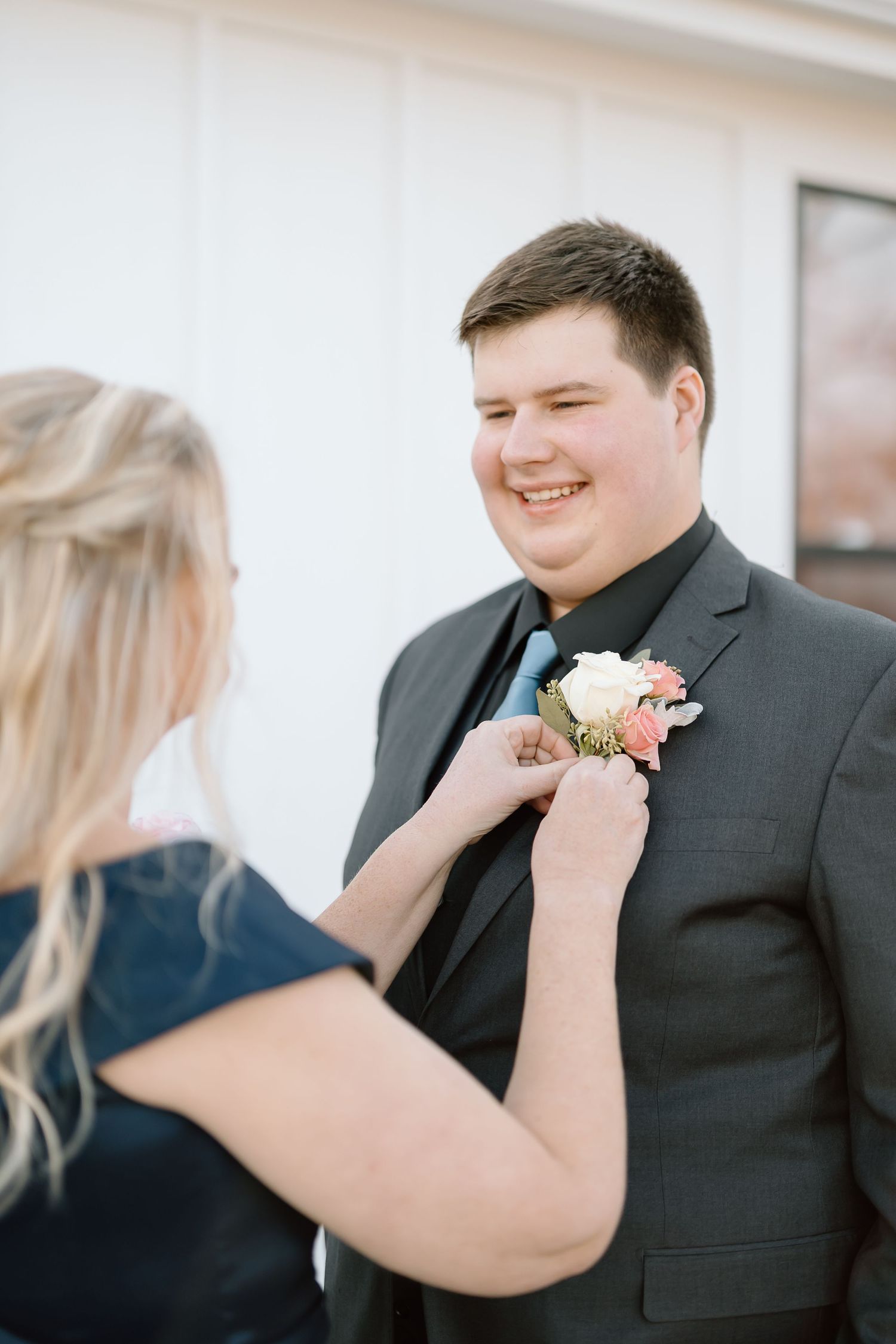 Someone pins a white and pink floral boutonniere onto a dark suit jacket in a series of candid moments.