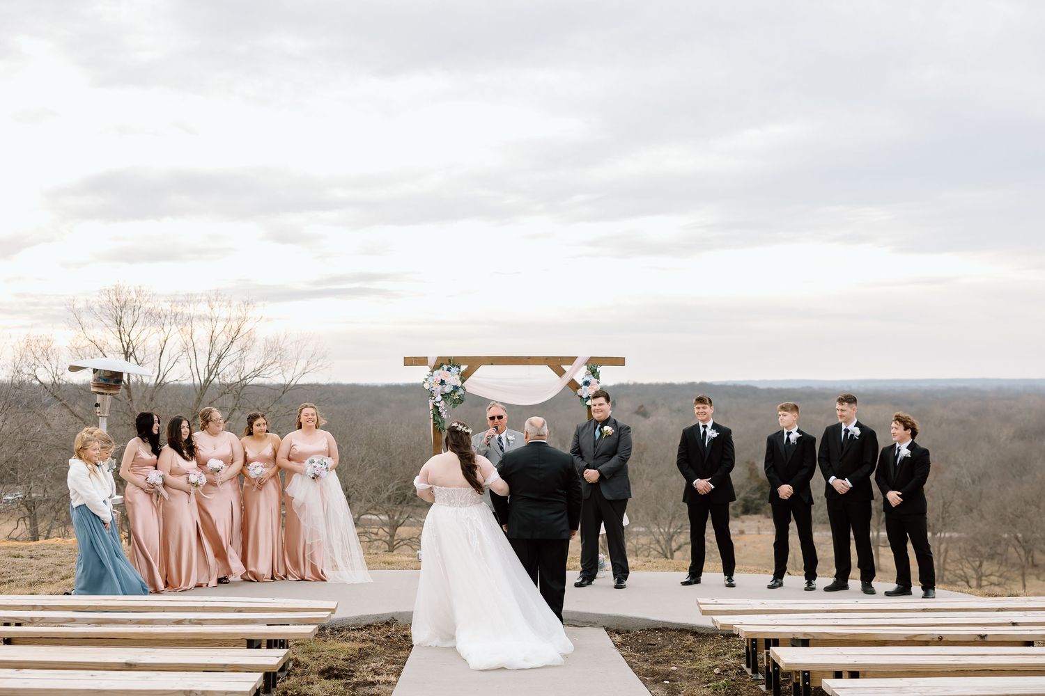 A wedding party stands in line on a scenic overlook during a cloudy day in the mountains.