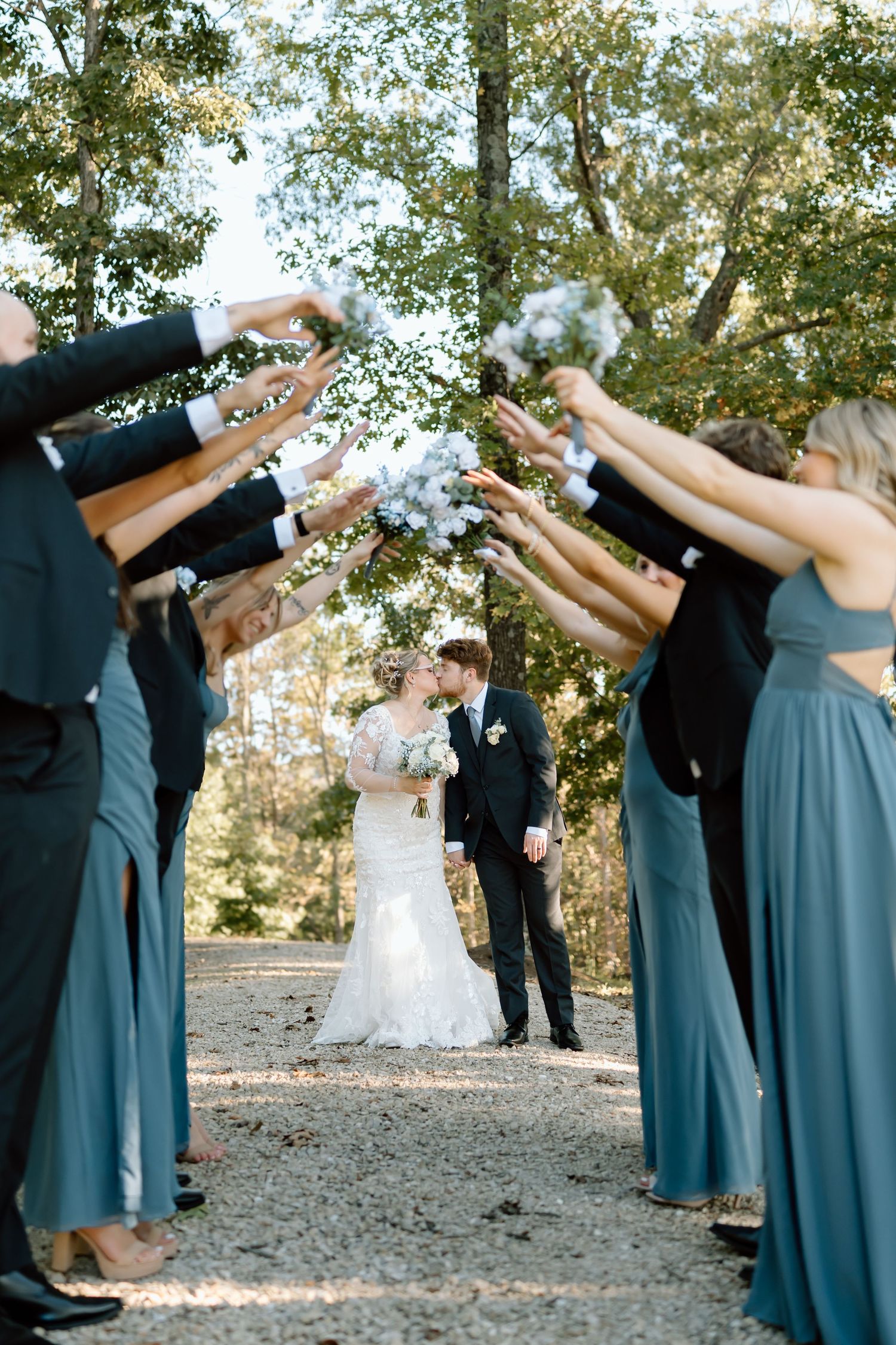 Wedding party members in blue dresses and suits perform a synchronized dab dance move during outdoor celebration.