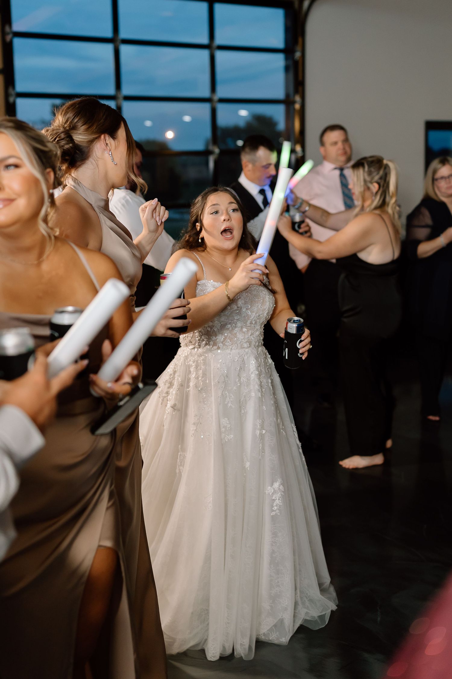 Wedding party dancing and celebrating on a dark dance floor with a bride in a sparkly white gown.
