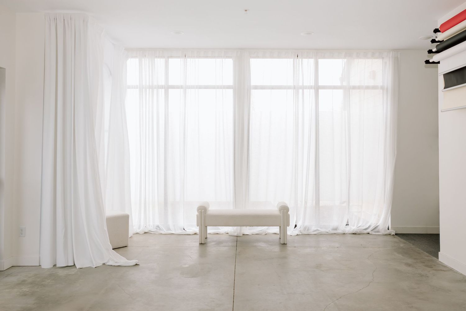 Modern white curtains filter natural light through large windows in a bright, minimalist interior space.