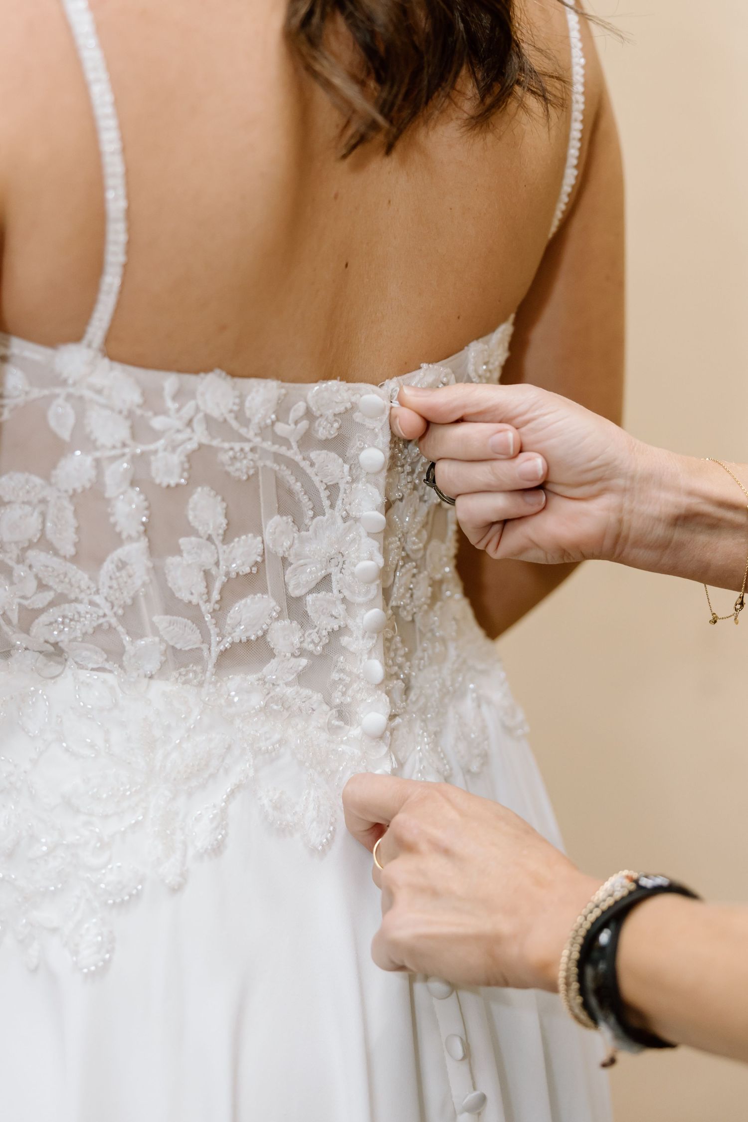 Close-up view of hands adjusting delicate white lace details on a wedding dress bodice.