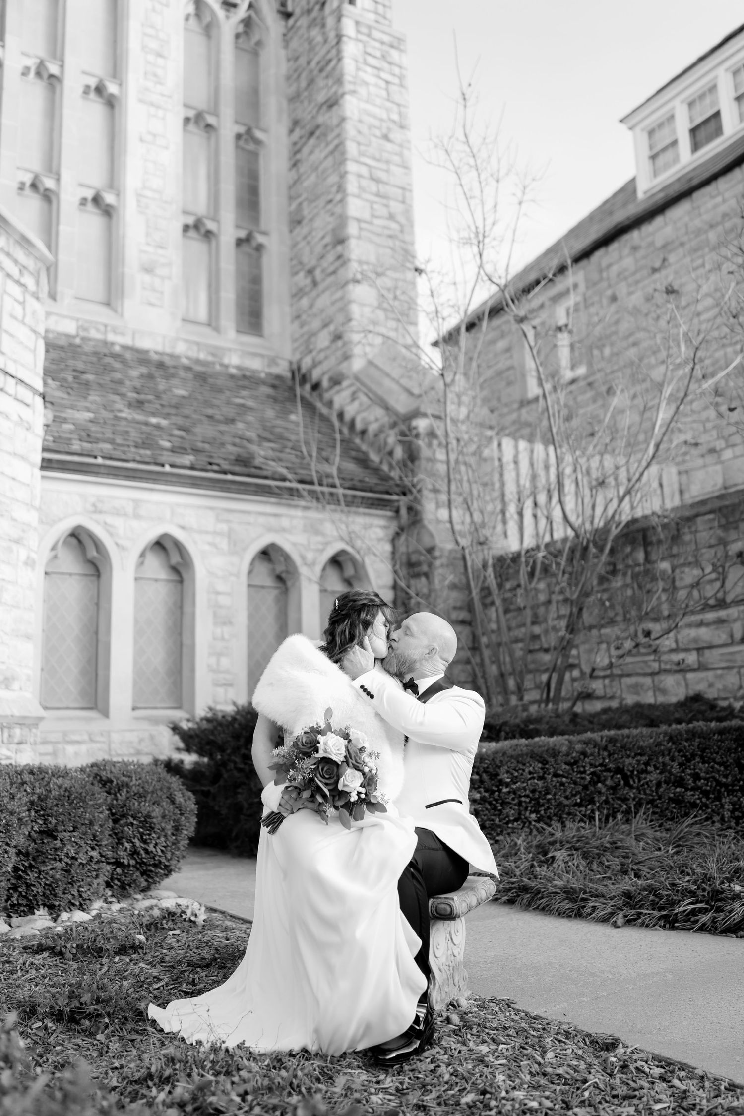 A romantic wedding moment captured in black and white outside a stone church with Gothic architecture.