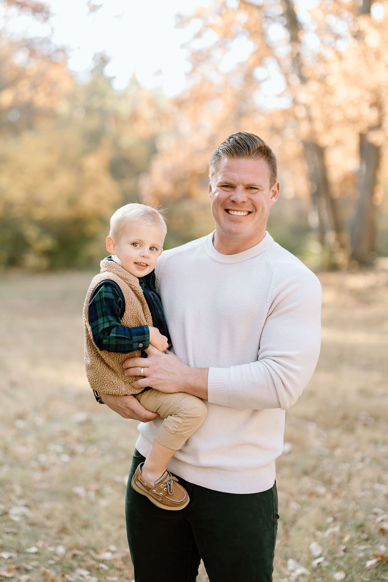 An outdoor portrait features a parent in white holding a child against a backdrop of fall trees.