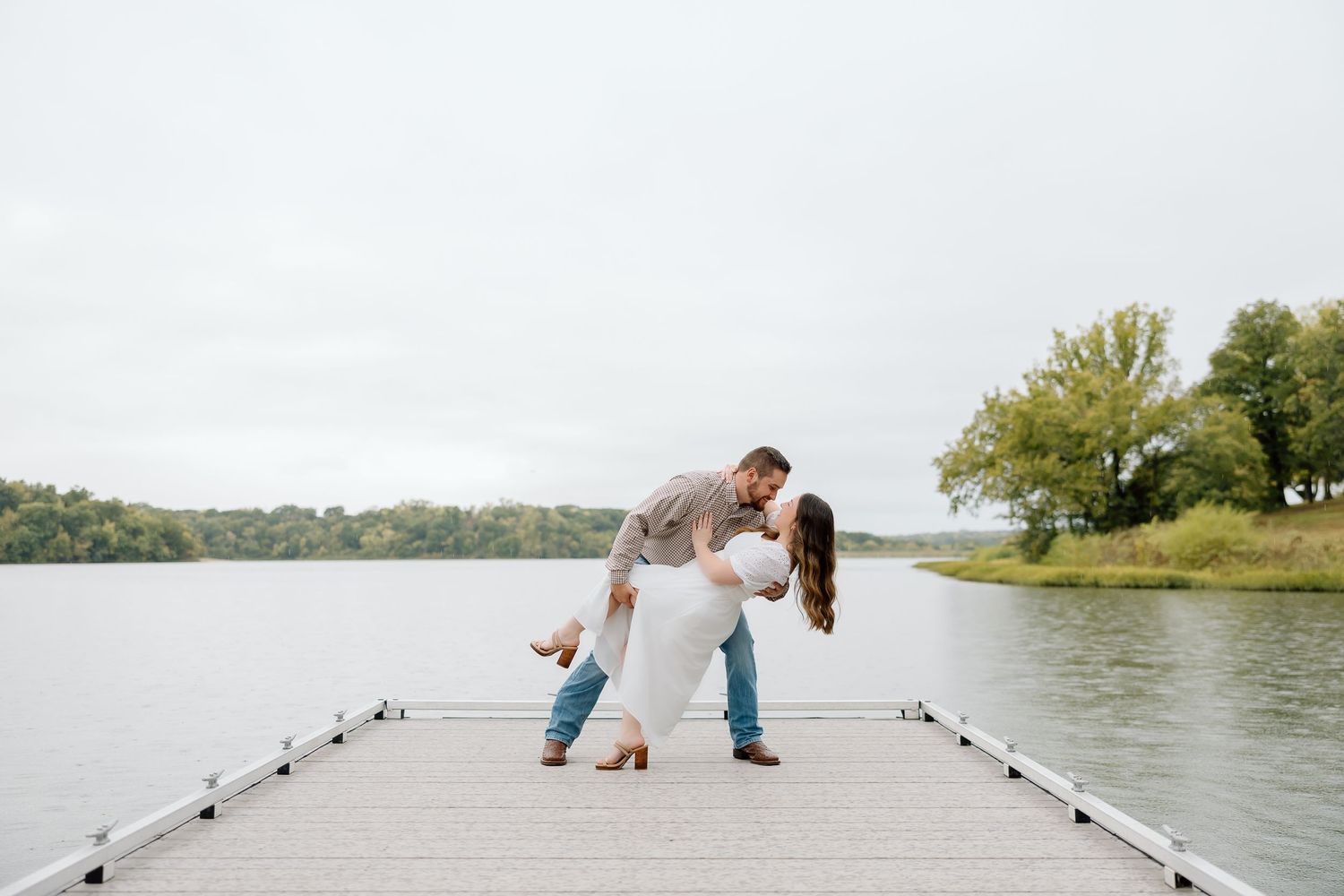 A playful couple poses on a wooden dock with a scenic lake backdrop.